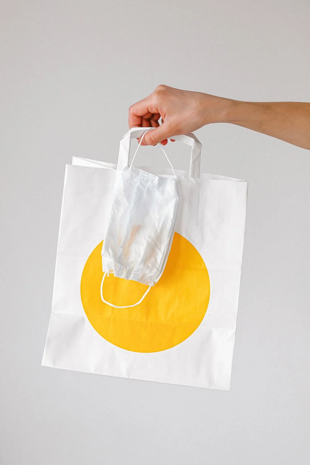 Mujer sosteniendo una bolsa de papel y una mascarilla con su mano. | Foto: Pexels