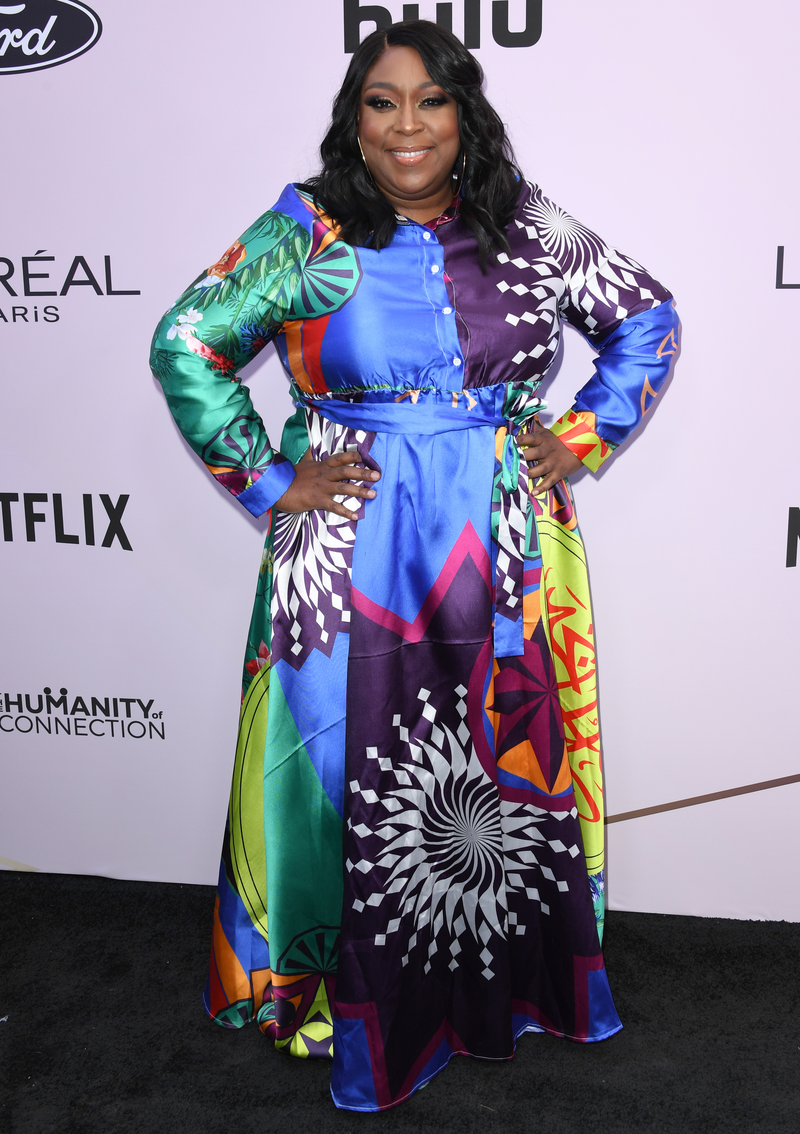 Loni Love attends the 13th Annual Essence Black Women in Hollywood Awards Luncheon on February 6, wearing a bold, colorful satin dress with her hands on her hips.
