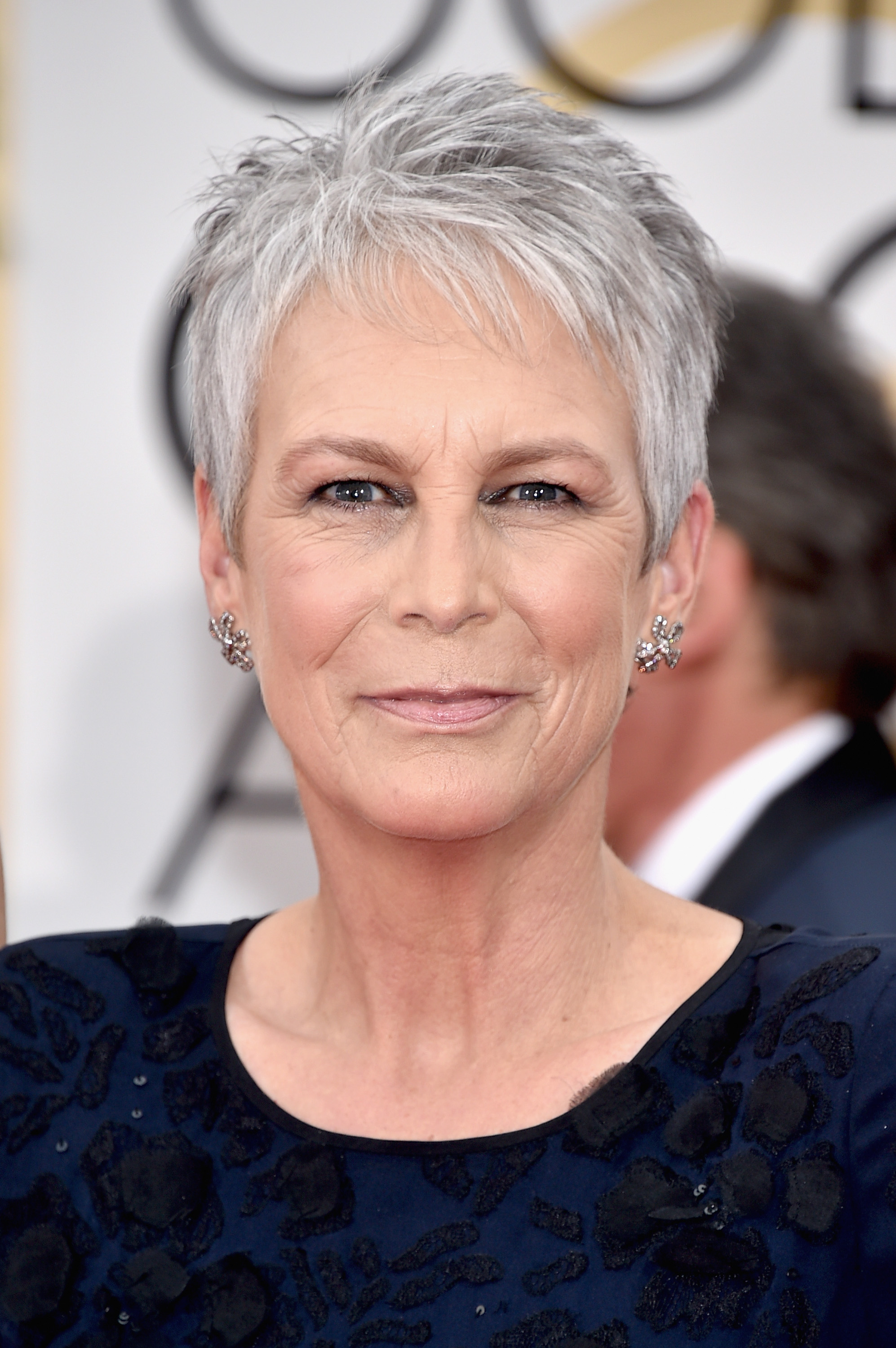 Jamie Lee Curtis attends the 73rd Annual Golden Globe Awards in a navy embroidered gown, her soft makeup and icy silver pixie cut highlighting her graceful red carpet presence.