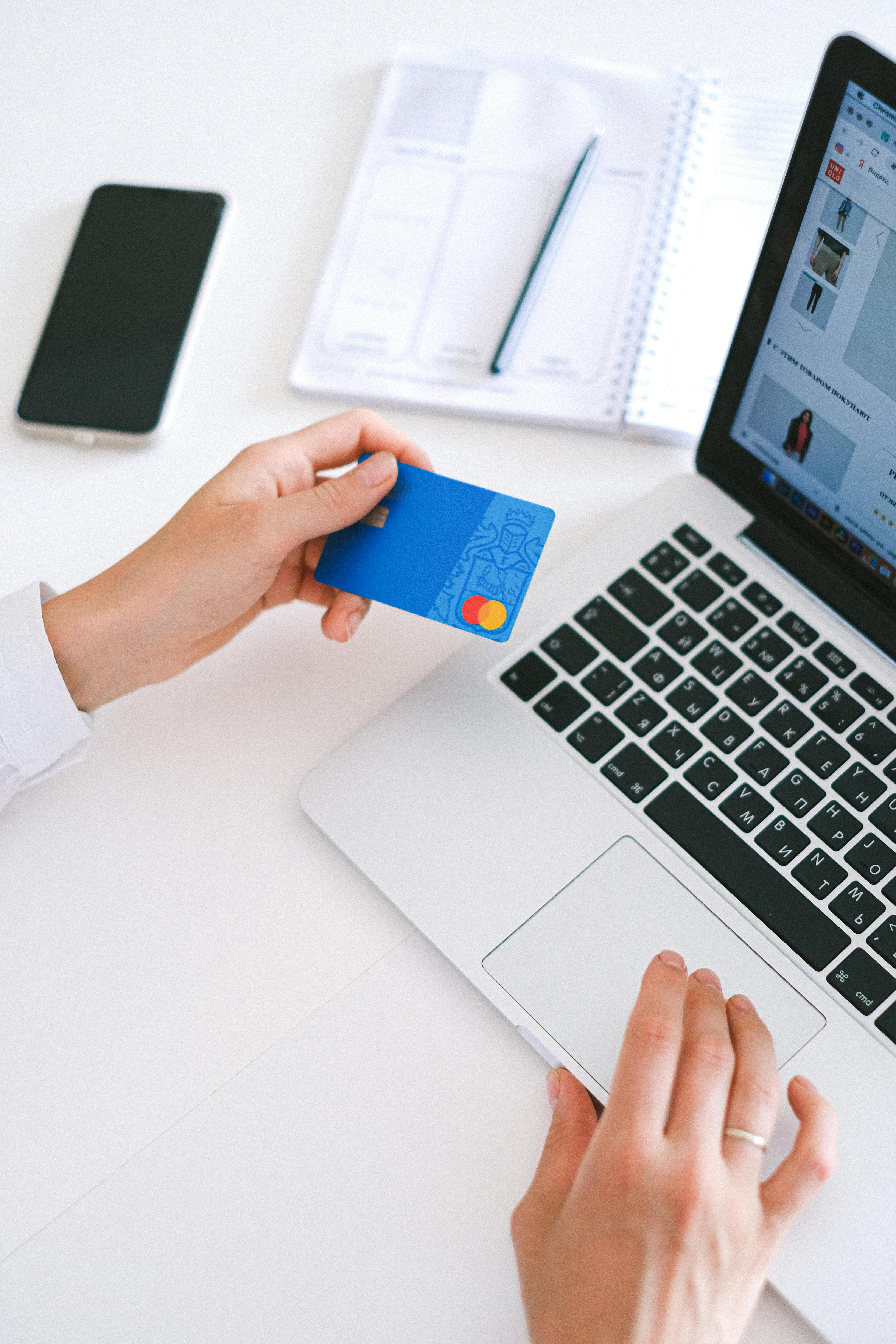 A woman holding a bank card with a laptop computer in the background | Source: Pexels