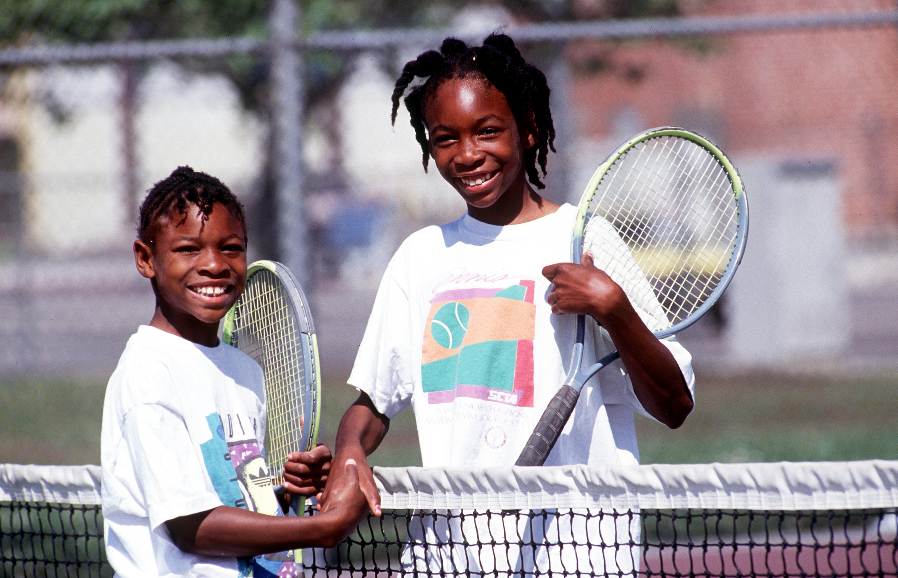 In April 1991, Serena Williams was pictured after a practice match with her sister Venus Williams. She wore a white tennis outfit and smiled as she shook hands across the net.