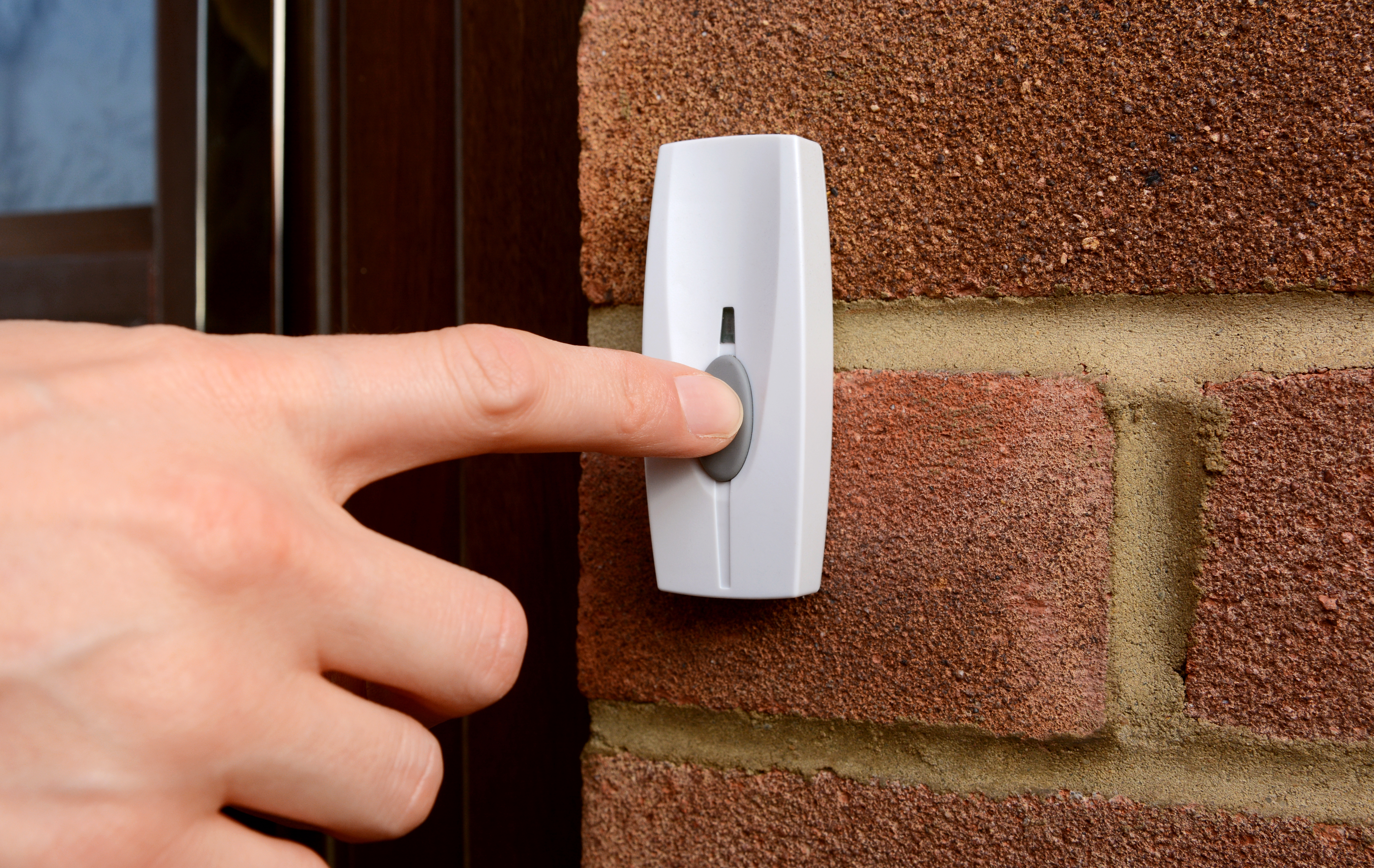 Close-up of woman pressing the button of a doorbell on a brick wall | Source: Shutterstock