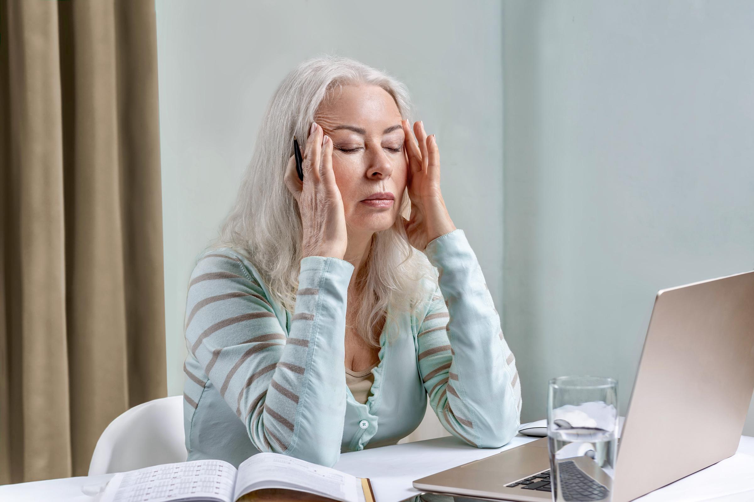 Woman rubbing her temples while seated at her work desk | Source: Shutterstock