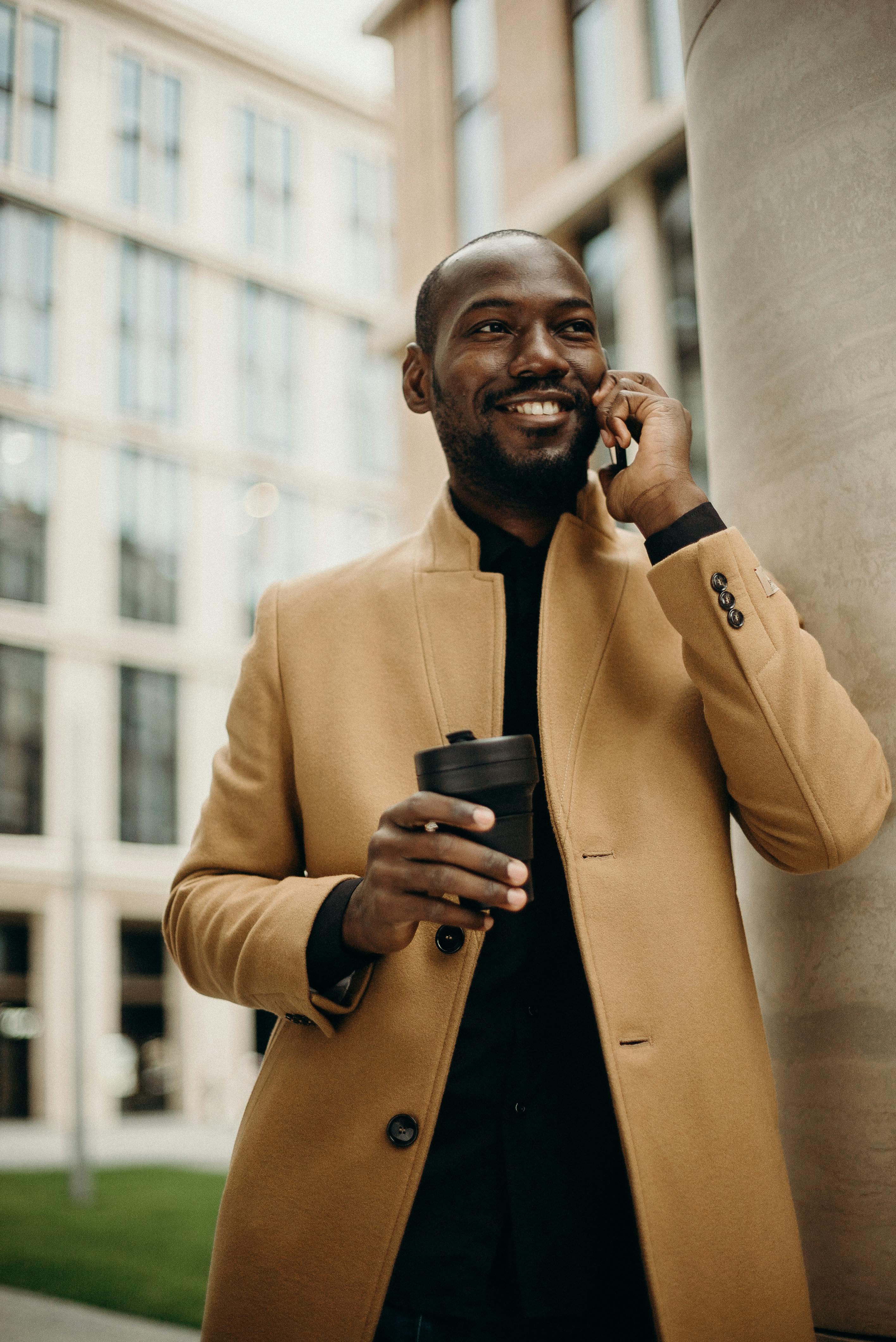 A happy man holding a beverage and talking on the phone | Source: Pexels