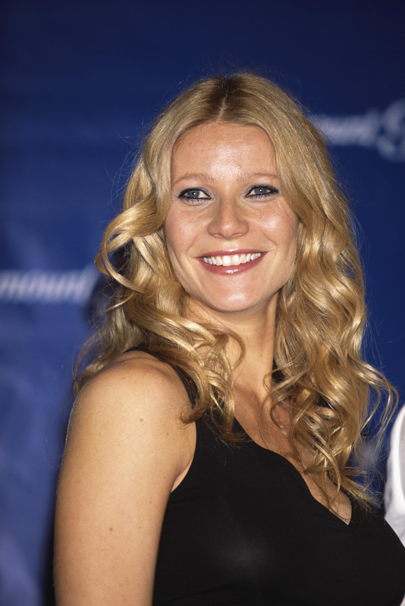 Gwyneth Paltrow smiles brightly in a head-and-shoulders portrait, her long blonde hair styled in soft curls as she faces forward with a relaxed expression at an earlier public appearance.