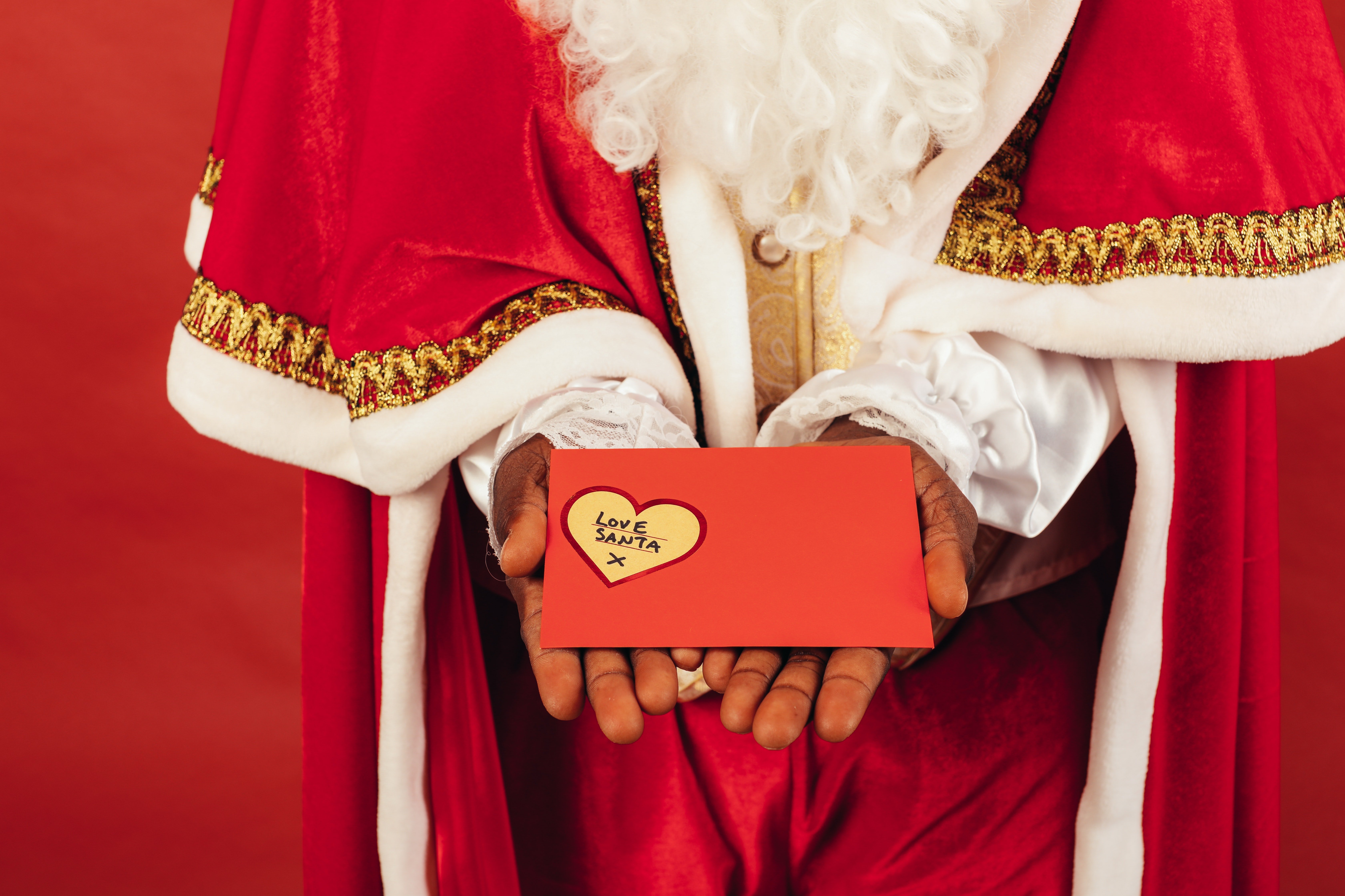 A person wearing Santa's outfit and holding a red envelope with a heart inscription on it. | Photo: Pexels