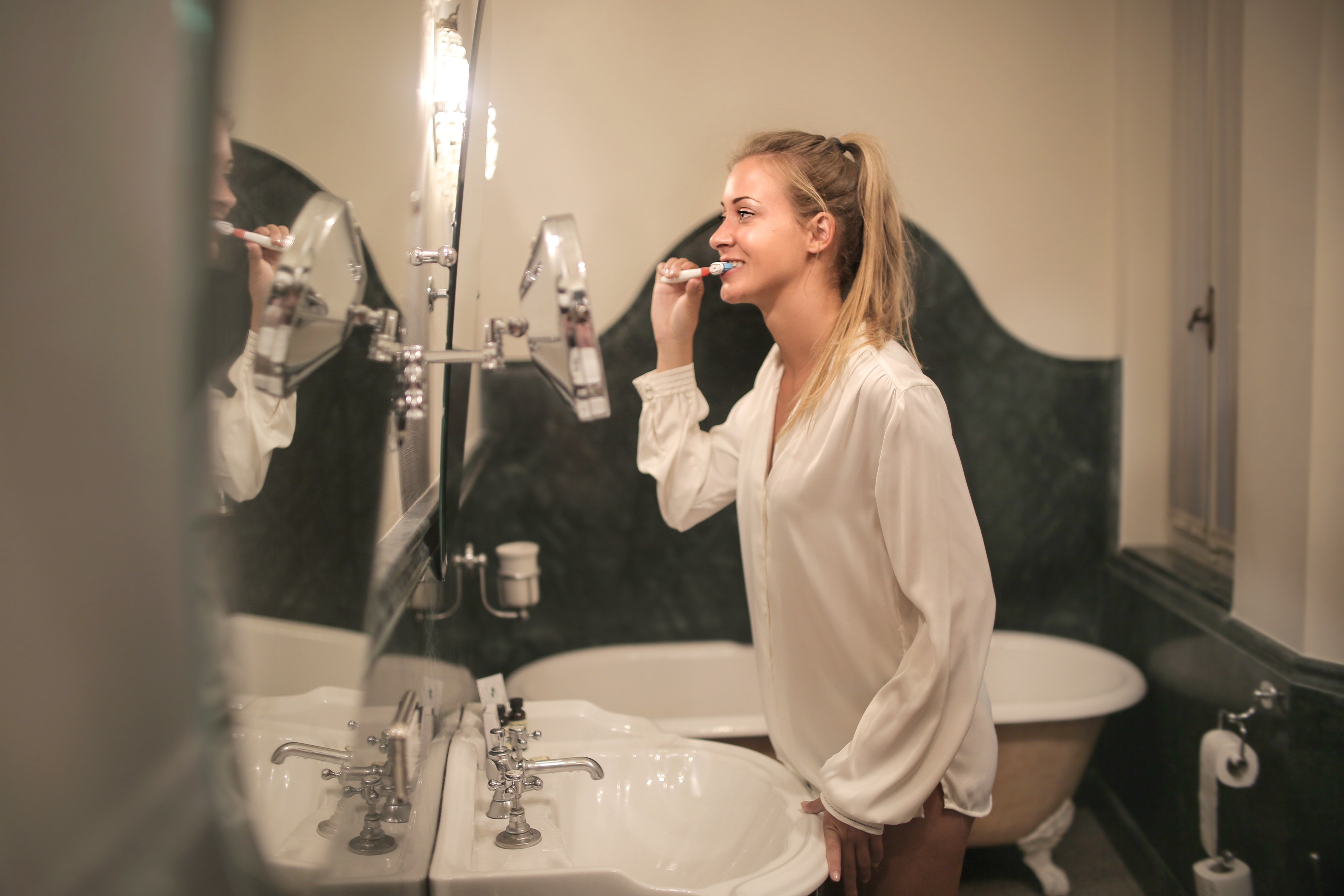 A woman stands by her basin and is busy brushing her teeth while she looks in the mirror | Photo: Pexels/Andrea Piacquadio 