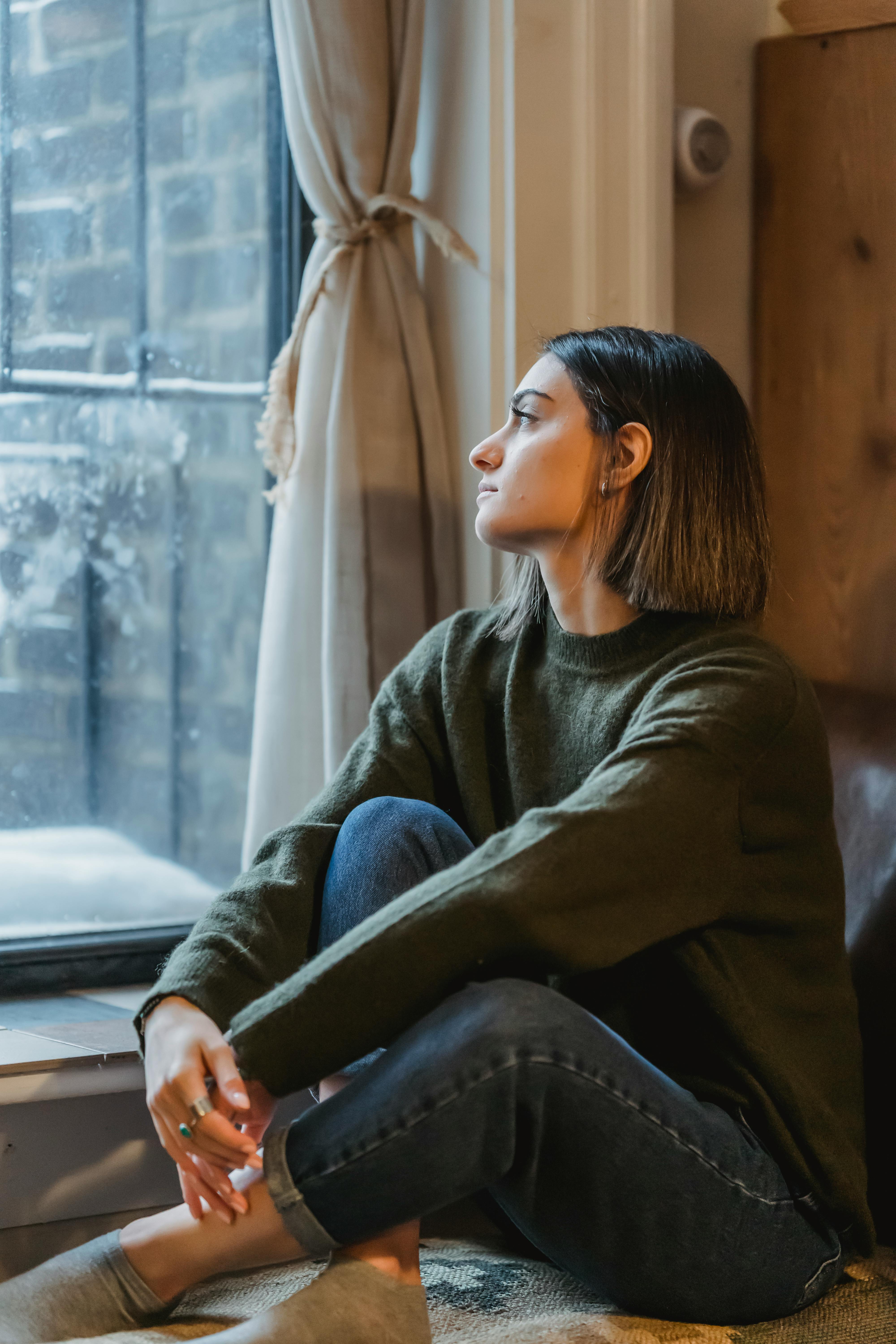 A young woman looking thoughtfully out of a window | Source: Pexels