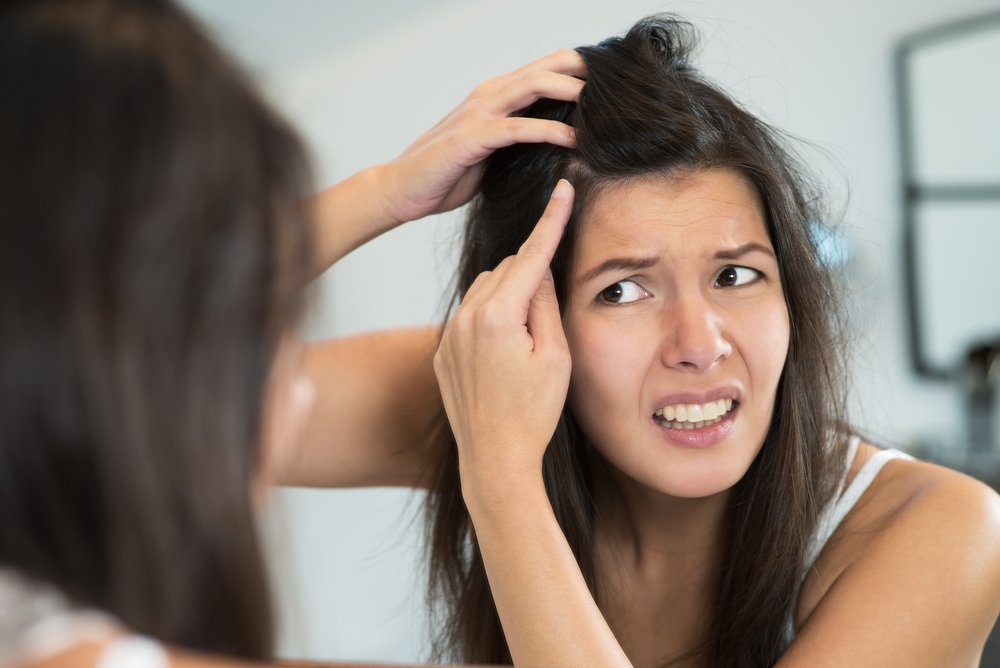 Young woman looking in the bathroom mirror at her scalp. | Source: Shutterstock