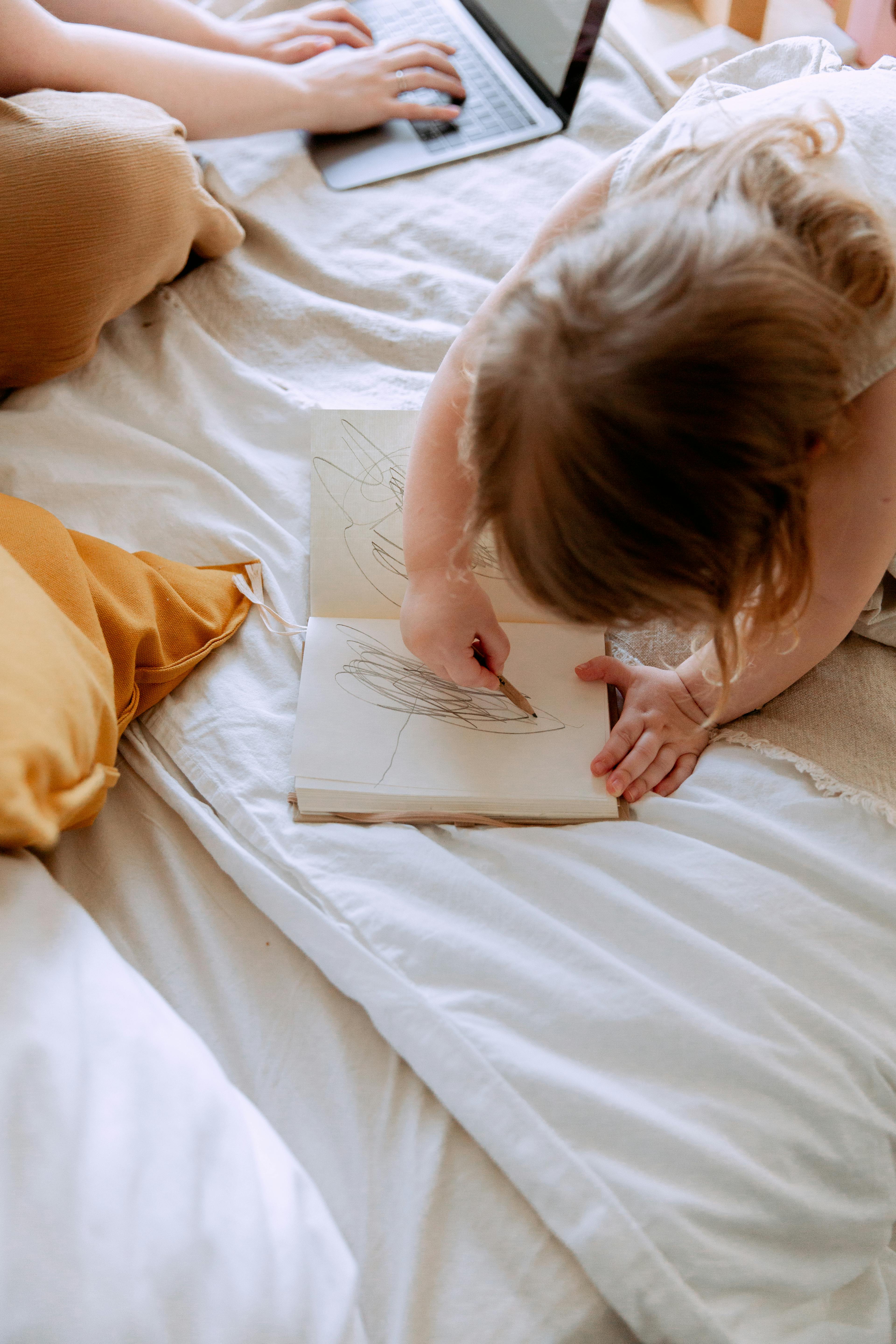 Kid draws in a notebook by his mom | Source: Pexels