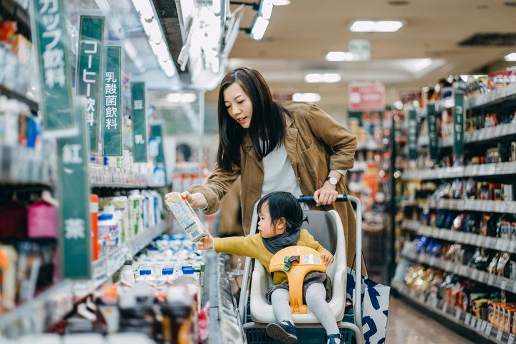 Cute little daughter sitting in a shopping cart grocery shopping for dairy product with young Asian mother in a supermarket | Photo: Getty Images