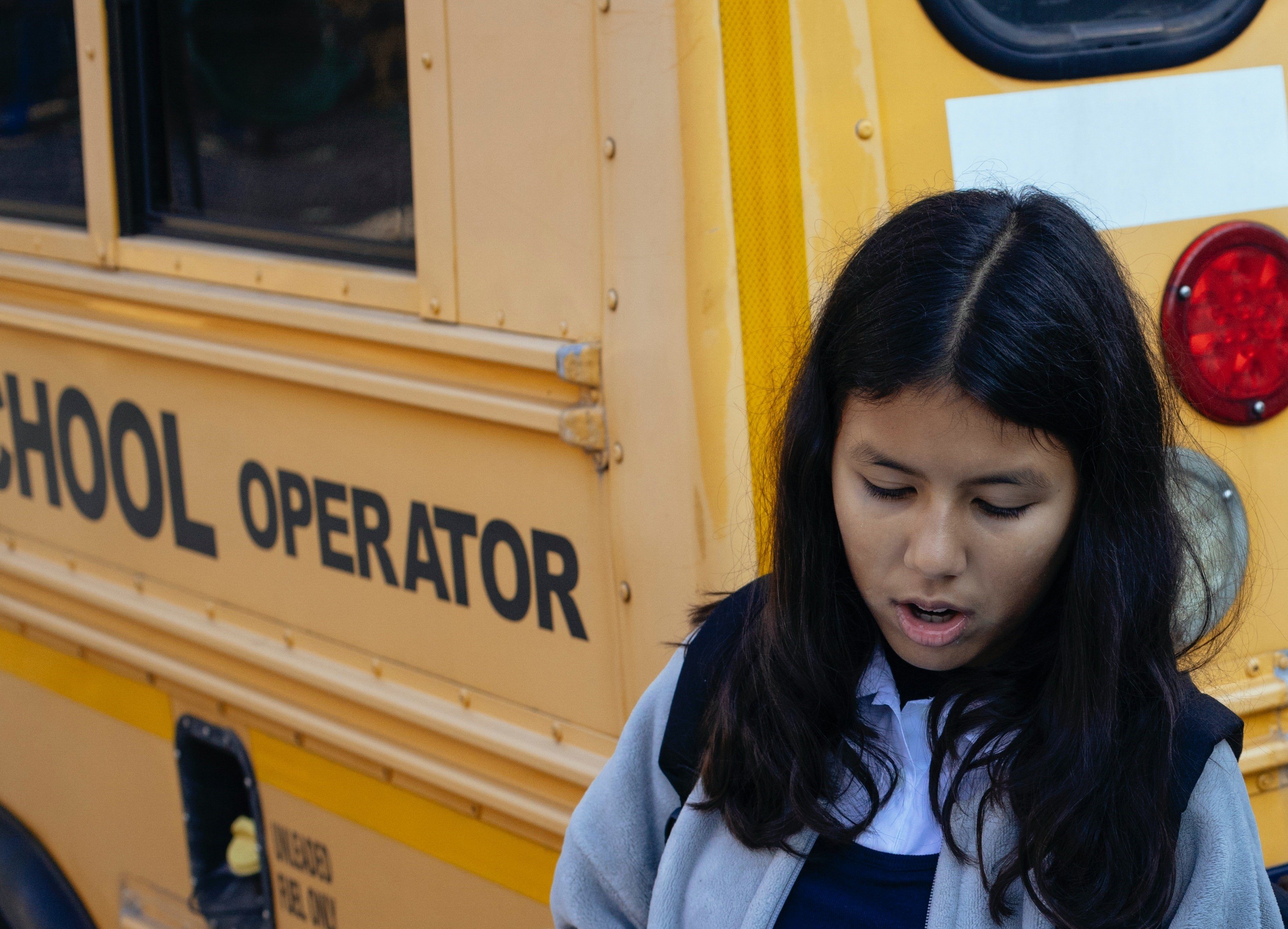 Una niña parada junto a un autobús escolar. | Foto: Pexels