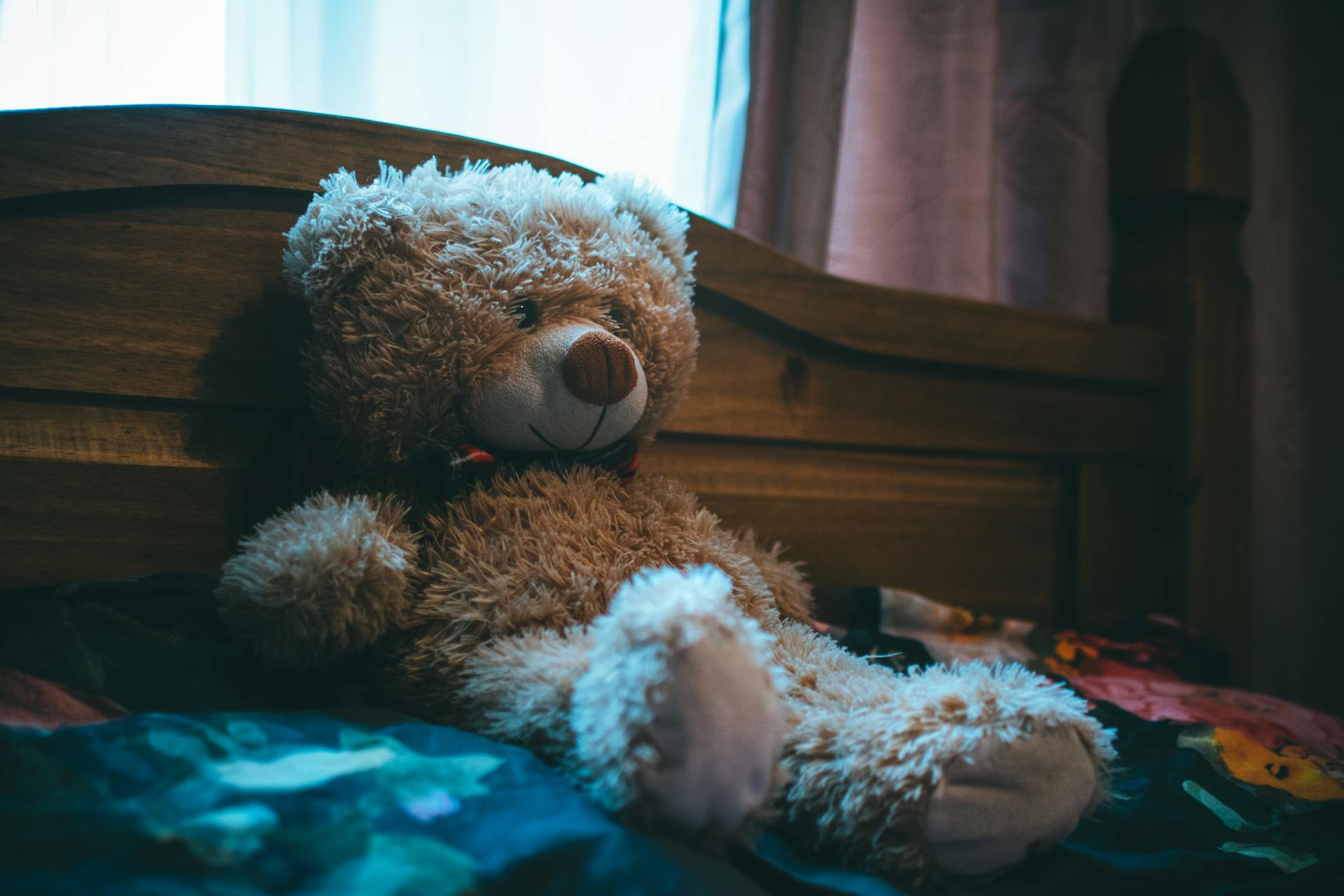 A fluffy brown teddy bear leaning on a bed headboard | Source: Pexels