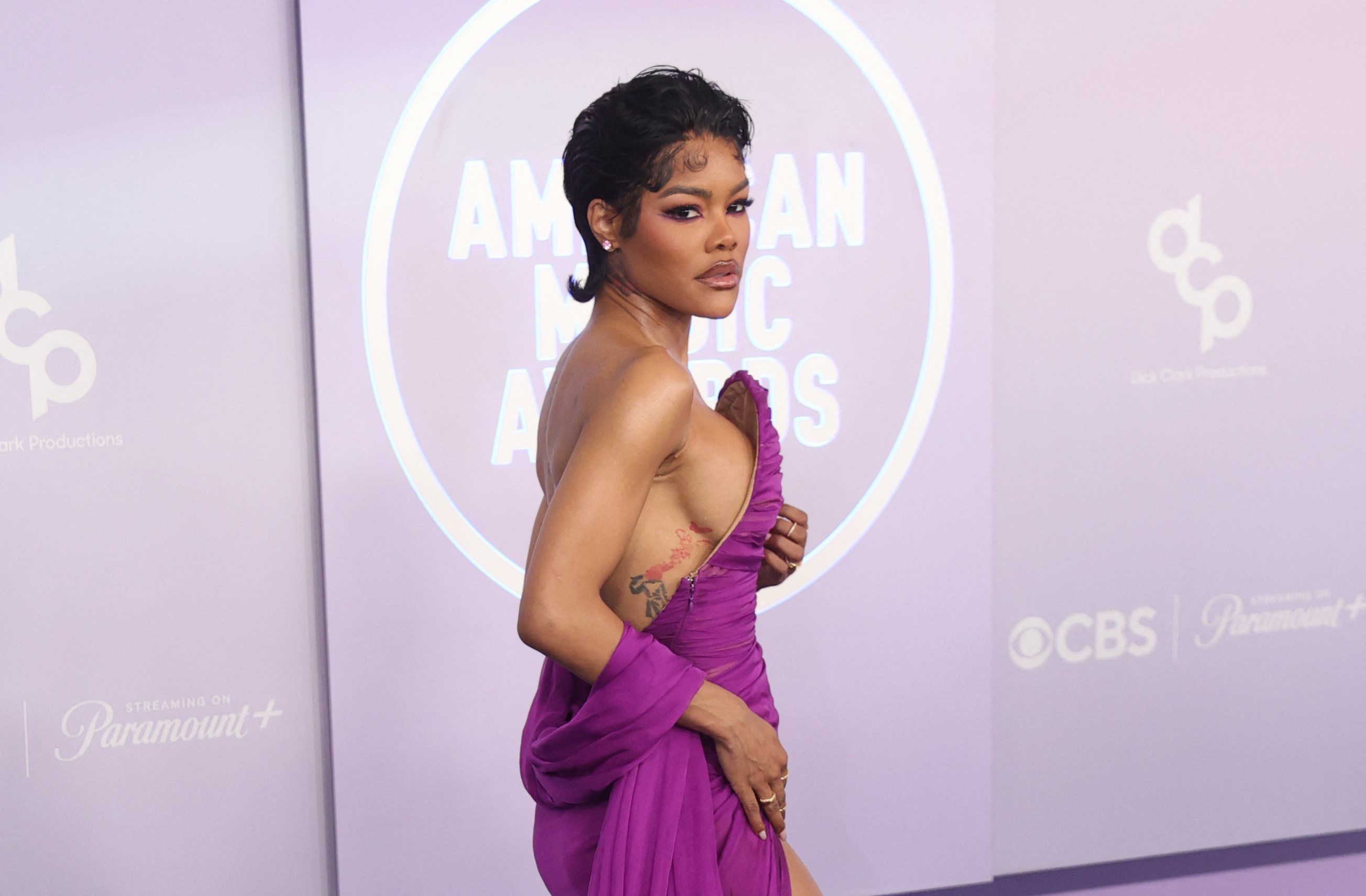 Teyana Taylor looks over her shoulder while posing in a one-shoulder purple gown with gathered fabric wrapped around her arm | Source: Getty Images