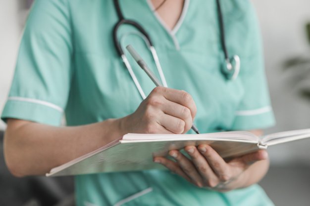 Mittelteil der Krankenschwester, die mit einem Stift auf Notizbuch schreibt | Quelle: Freepik