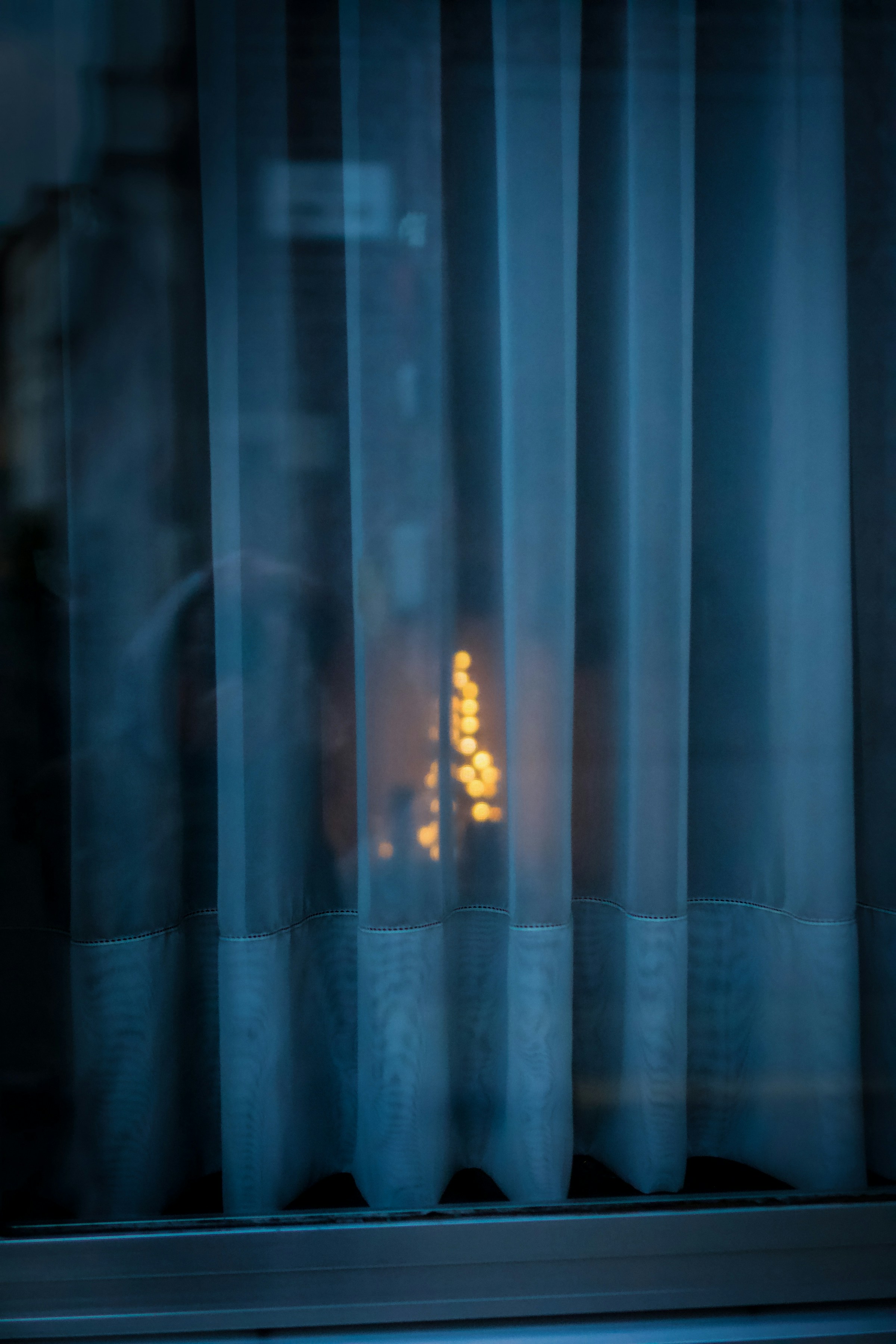 Christmas lights shining through a window curtain | Source: Unsplash