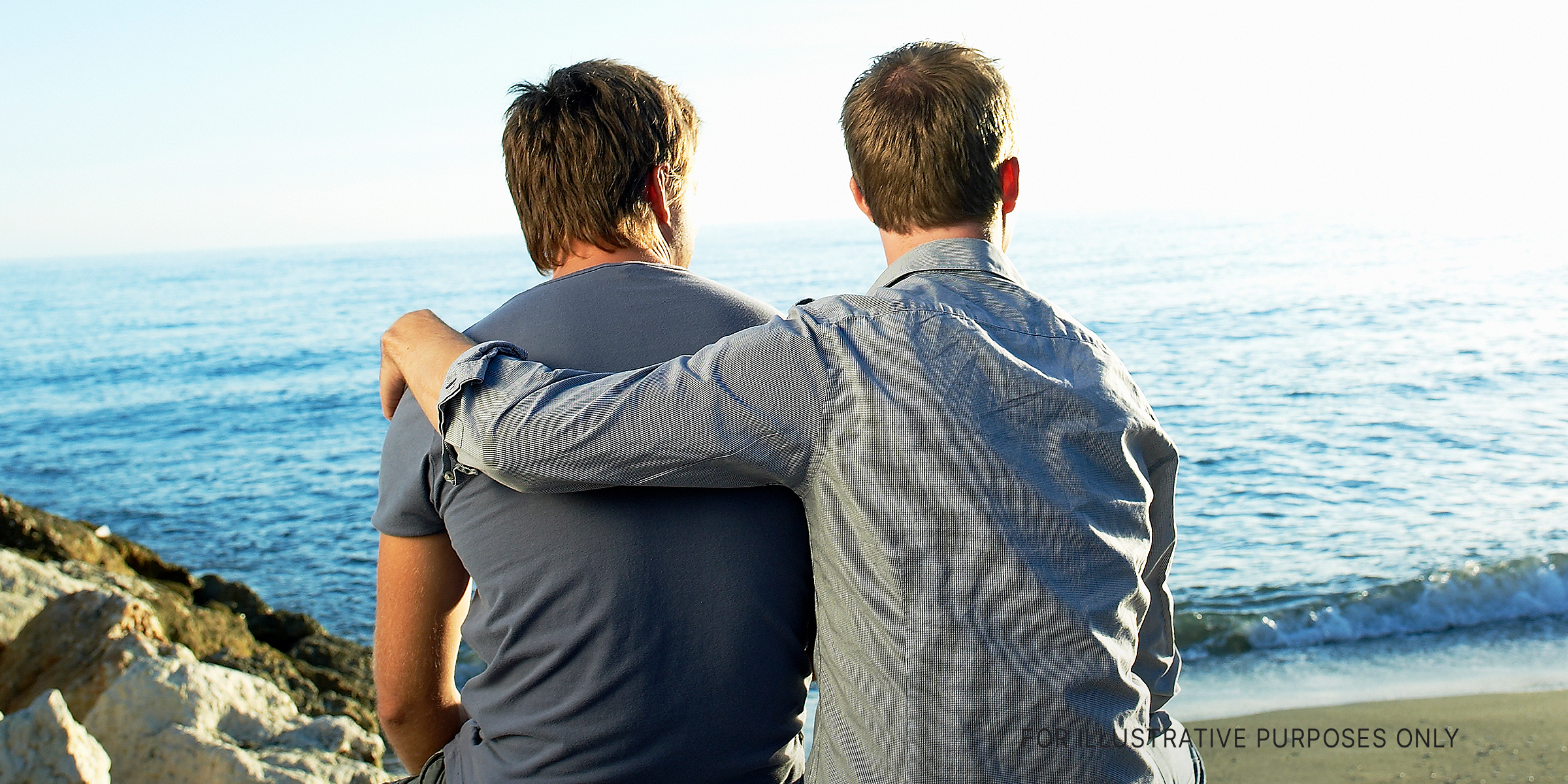 Two men looking at a view while one embraces the other | Source: Getty Images