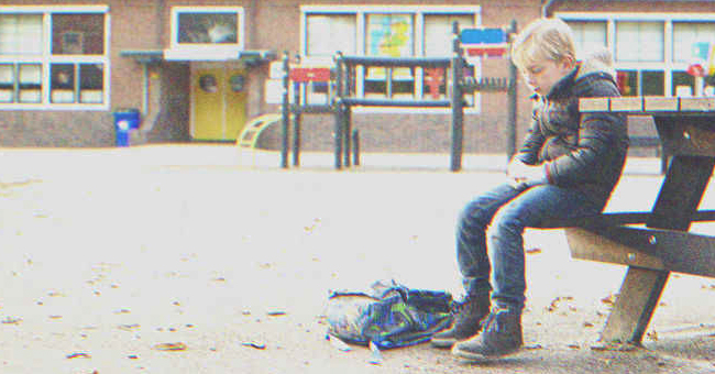 A boy sitting alone on a bench outside a school | Source: Shutterstock
