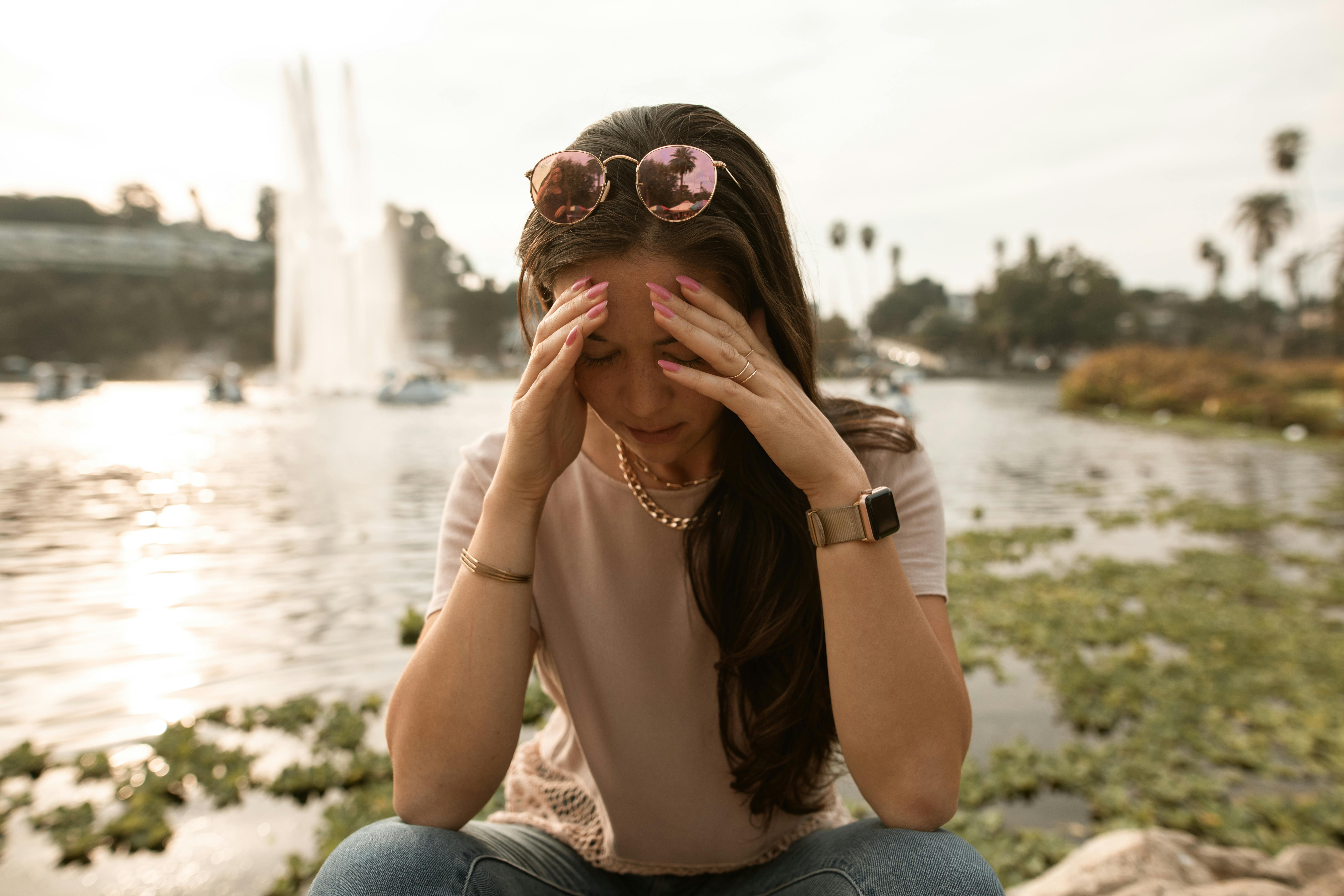 A distressed woman sitting on lakeside and touching her face in despair | Source: Pexels