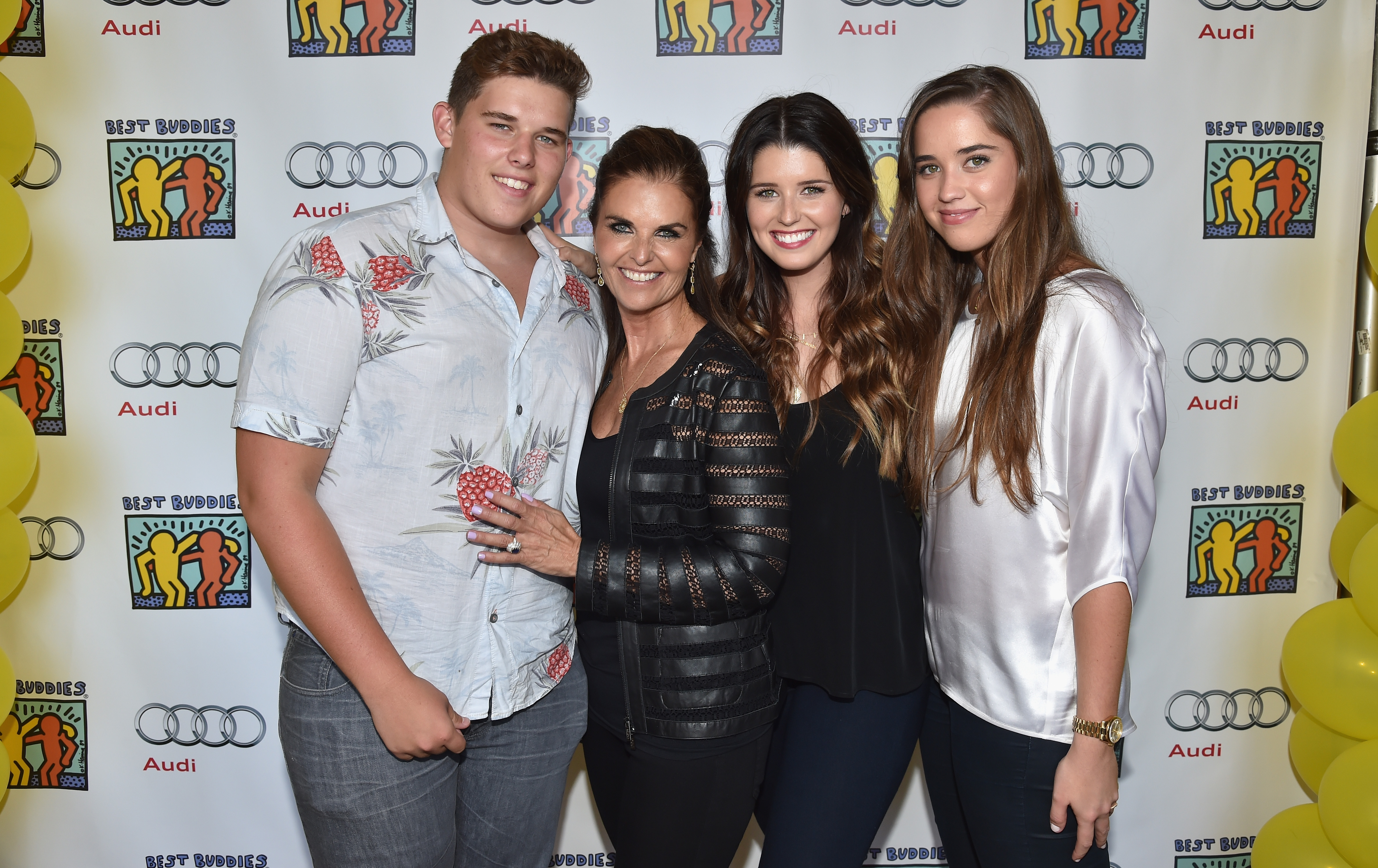 Christopher poses with his mom, Maria Shriver, and sisters Katherine and Christina at an event in Beverly Hills. Wearing a light button-down shirt with a bold fruit pattern and grey jeans, he stands confidently with a smile, his short hair neatly styled and his build visibly fuller at the time.