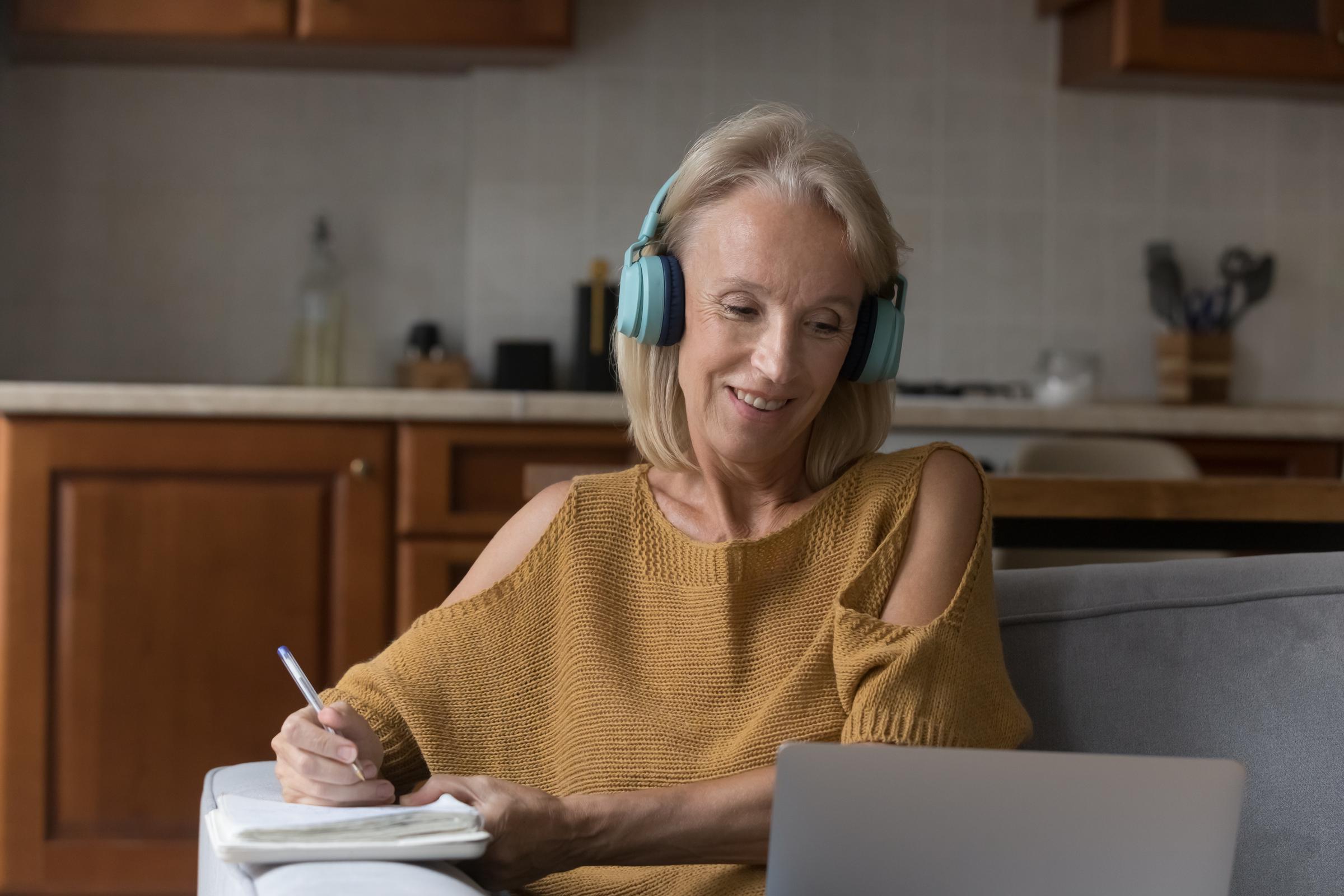 A woman wearing headphones and viewing her laptop while jotting down notes | Source: Shutterstocl