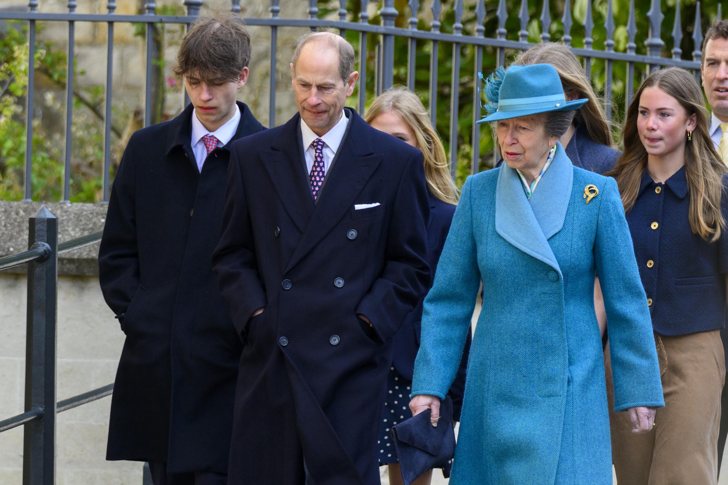 Prince Edward, Duke of Edinburgh, walks alongside his sister Princess Anne, the Princess Royal, as the family makes its way to St George's Chapel on 5 April 2026. Princess Anne is dressed in a teal wool coat and a matching feathered hat, a gold brooch pinned at her lapel, while James, Earl of Wessex, keeps pace just to his father's left.