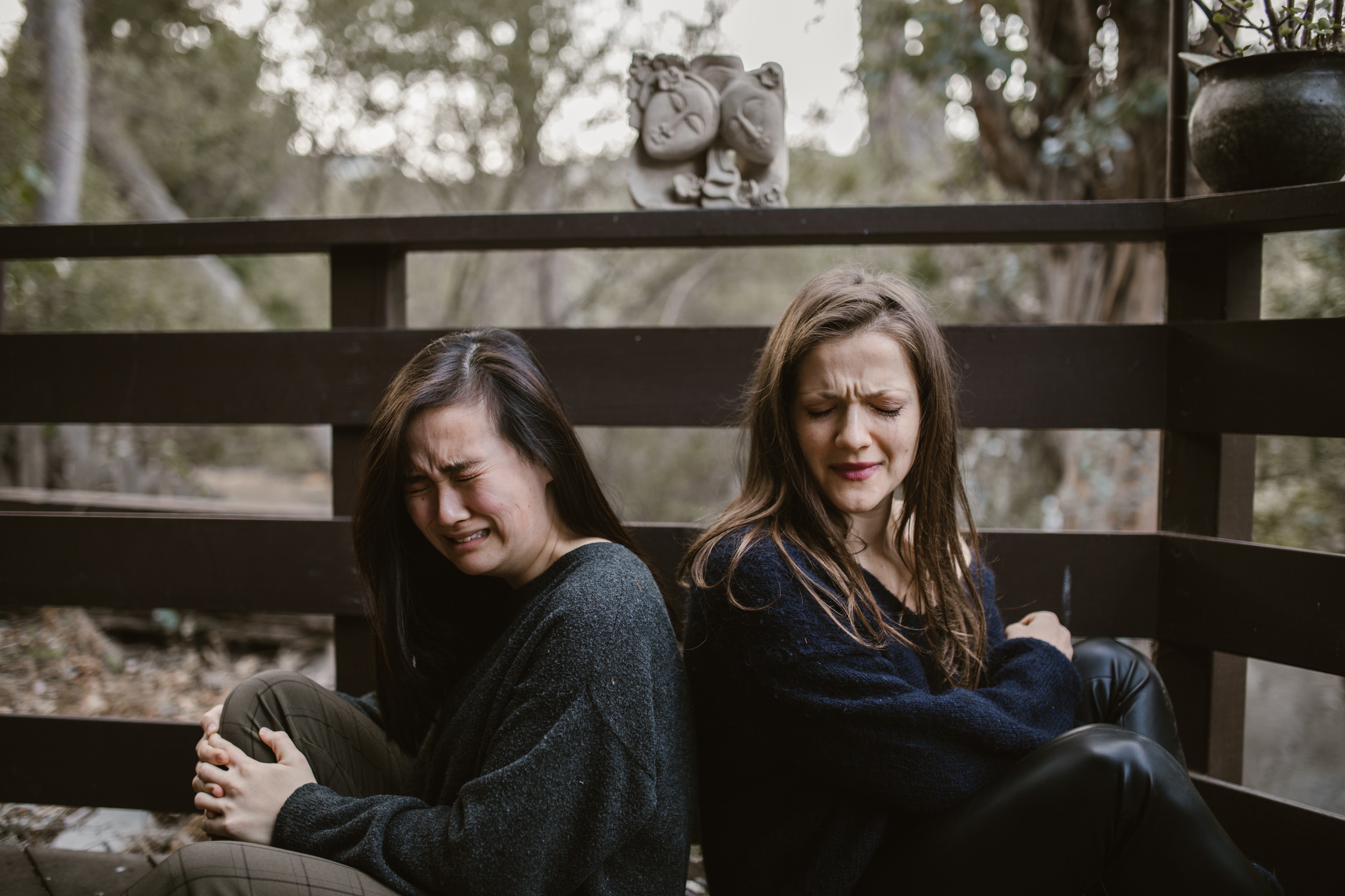 Pictured - Two young women sitting on a bench with their backs against each other crying | Source: Pexels 