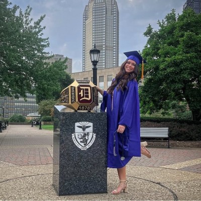 Madeline Spatafore poses in her graduation cap and gown beside a Duquesne University emblem on campus. | Source: LinkedIn/Madeline Spatafore