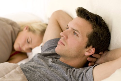 A worried man next to his sleeping wife in bed. | Source: Shutterstock.