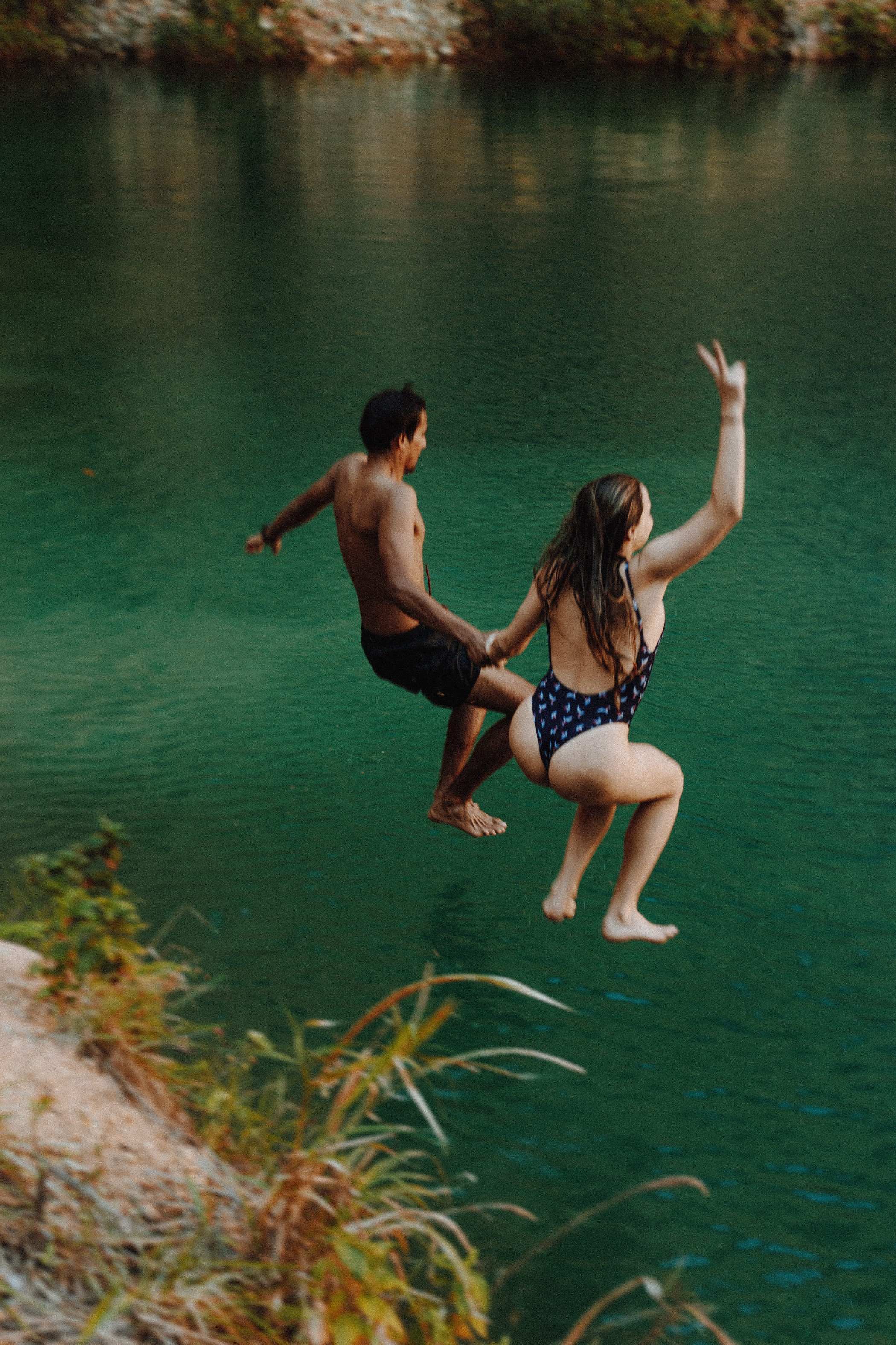 A couple jumping off a cliff into water together. | Source: Pexels