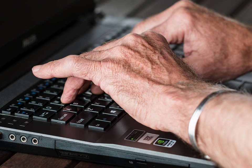 Manos de un anciano escribiendo con el teclado de una computadora portátil. | Foto: Pixabay