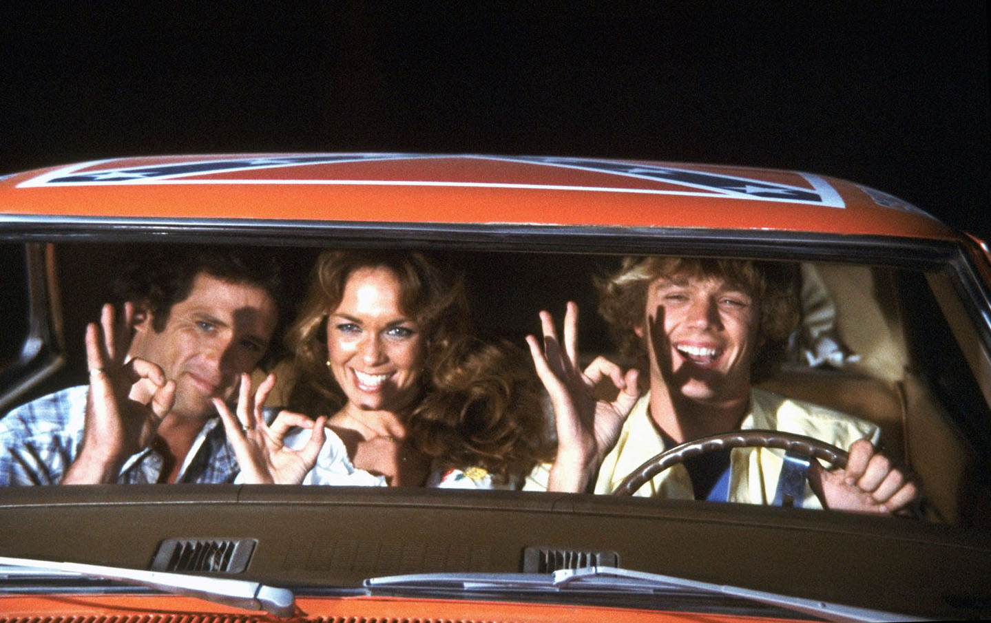 Wopat, Bach and Schneider share the front seat of the General Lee in this early cast image, underscoring how closely the three leads were tied to the show's signature car. Their easy chemistry became a major part of the series' appeal. | Source: Getty Images