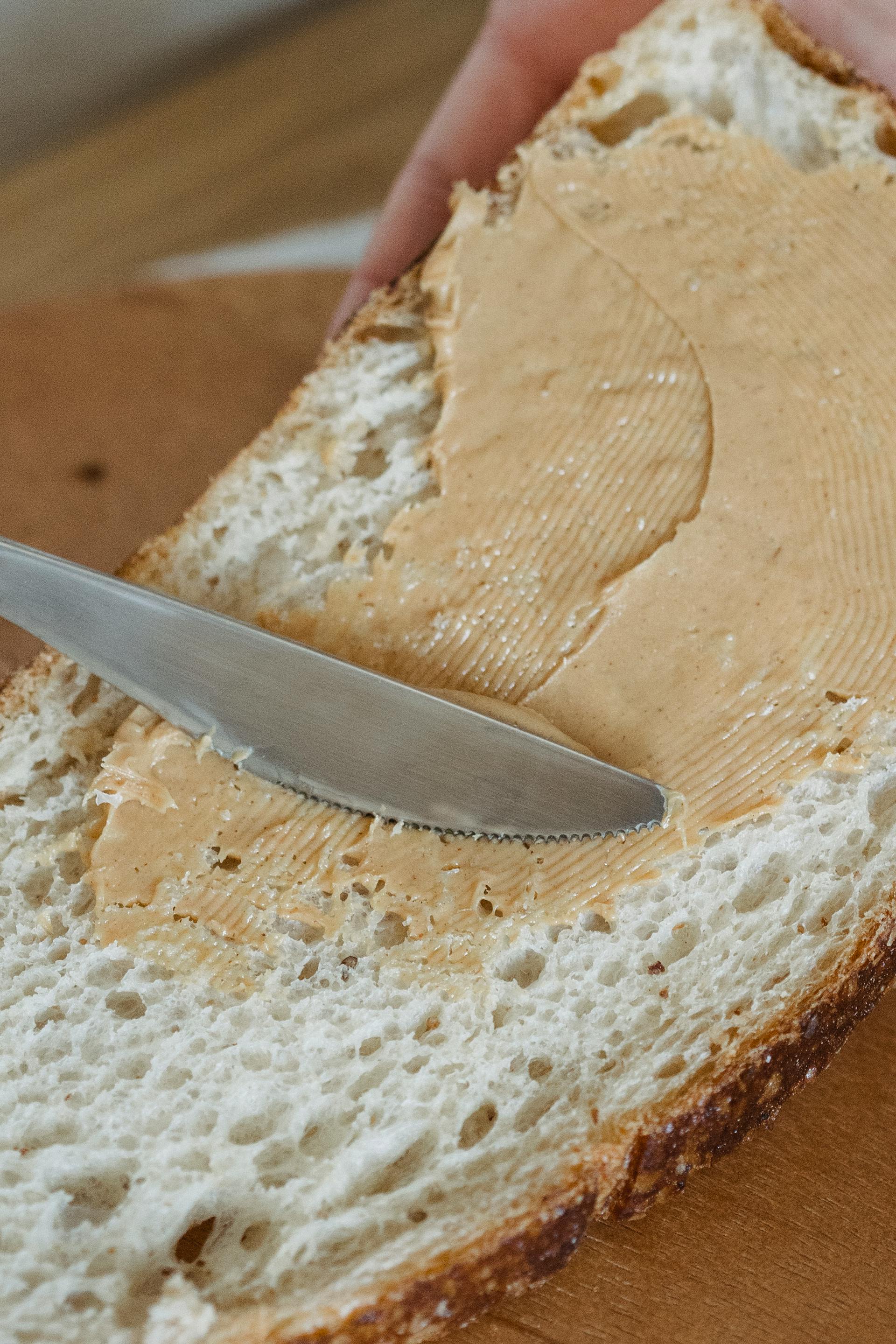 Close-up shot of a person spreading peanut butter on a slice of bread | Source: Pexels