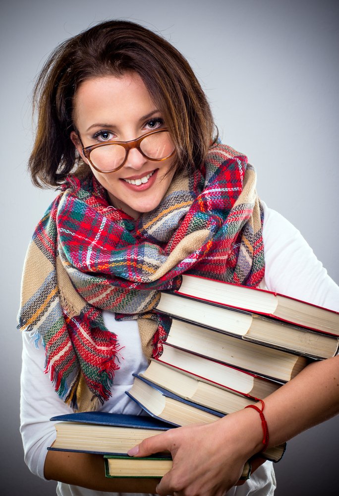 Mujer sosteniendo unos libros, usando anteojos y una bufanda de colores brillantes. | Foto: Shutterstock