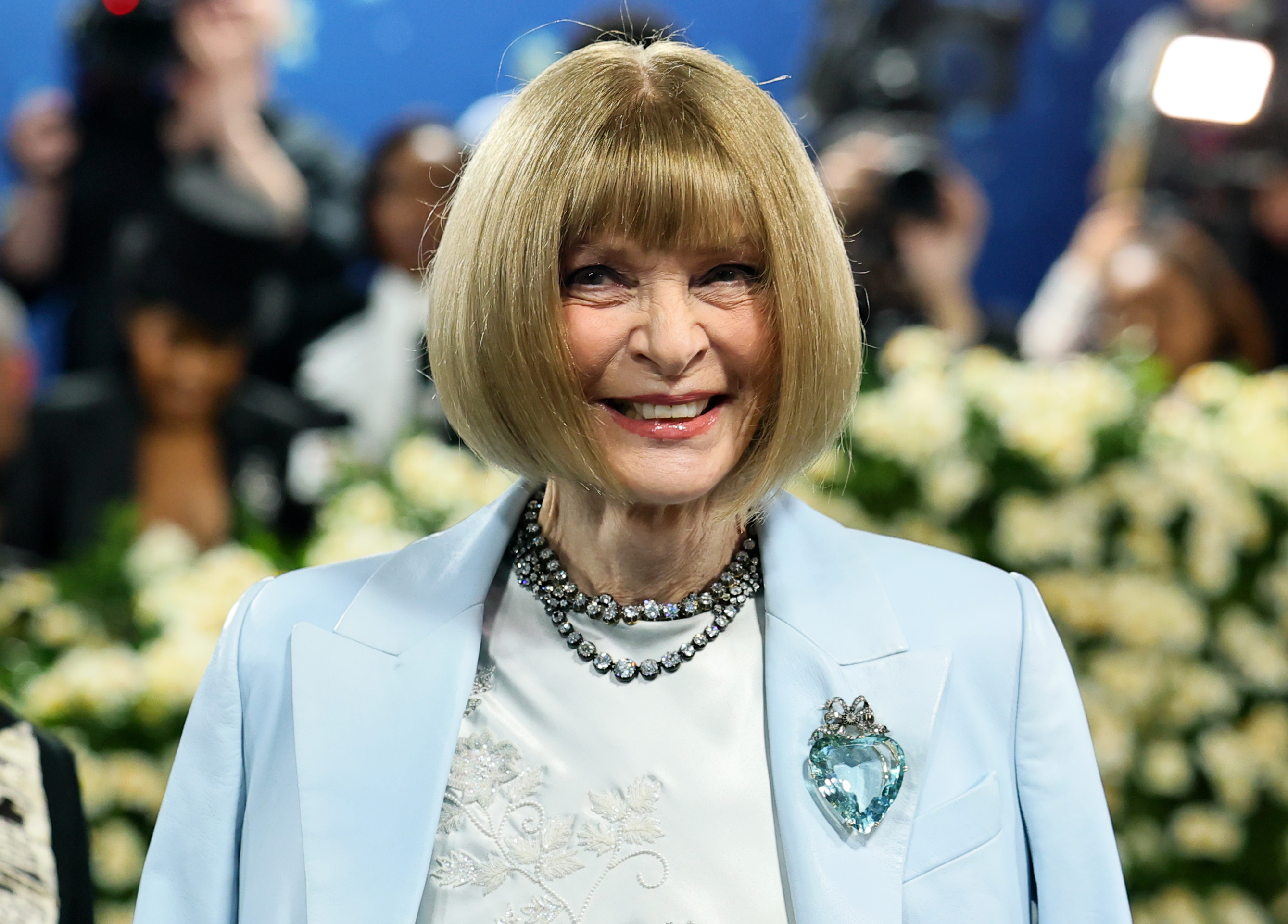 Anna Wintour beams as cameras flash around her at the 2025 Met Gala. Her signature bob, ornate necklace, and powder blue blazer complete her tribute to "Superfine: Tailoring Black Style" at the Metropolitan Museum of Art.