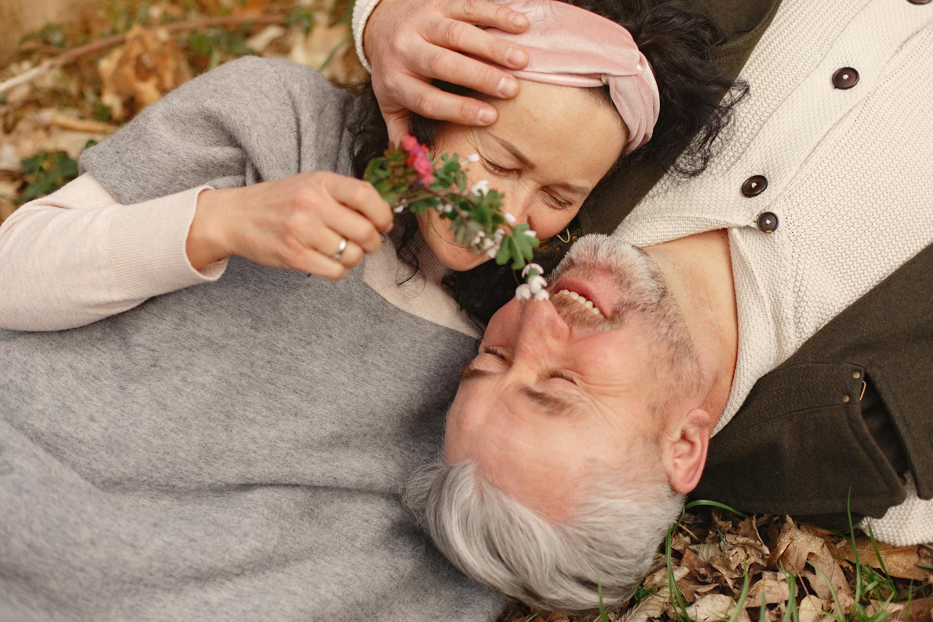 A senior couple cuddling while lying down on a bunch of fallen leaves | Source: Pexels