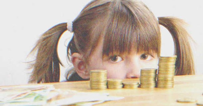 A little girl stands behind a counter with money. | Source: Shutterstock