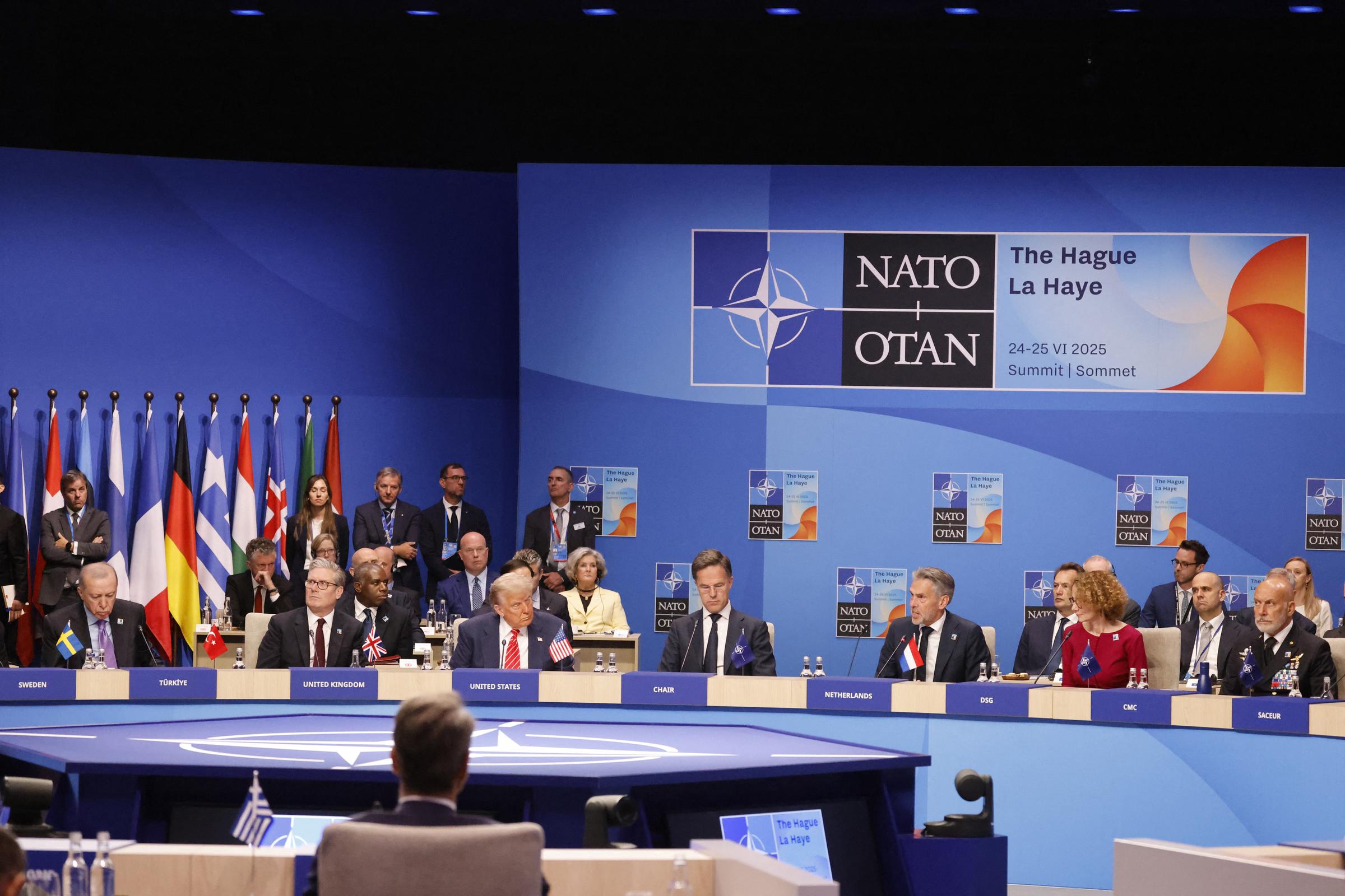 A wide shot captures a powerful scene as world leaders gather around a polished conference table, deep in discussion. Turkey's President Recep Tayyip Erdogan, Britain's Prime Minister Keir Starmer, Trump, NATO Secretary General Mark Rutte, and Schoof are all seated, their expressions serious and focused.