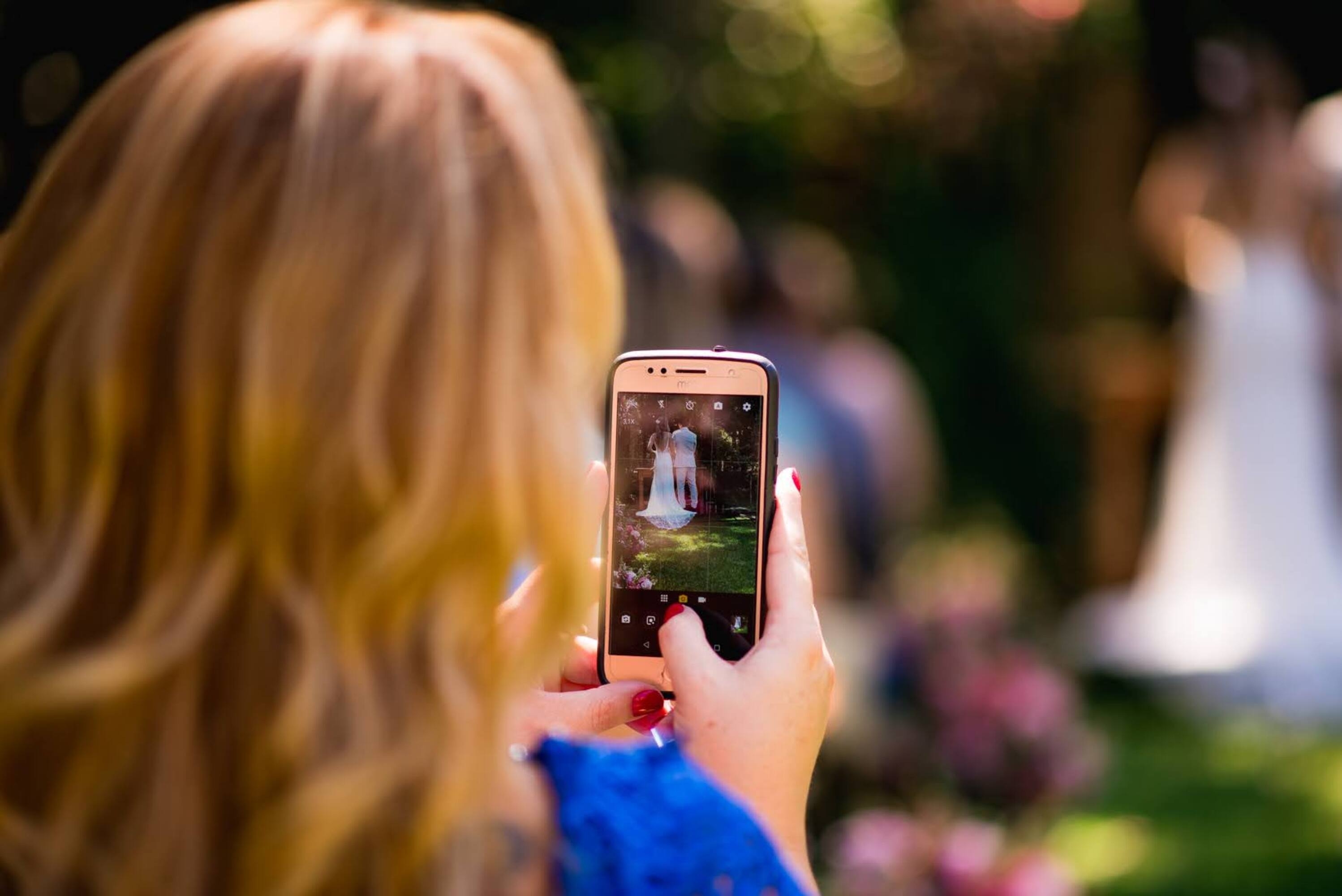A woman taking a photo with her phone at a wedding | Source: Shutterstock