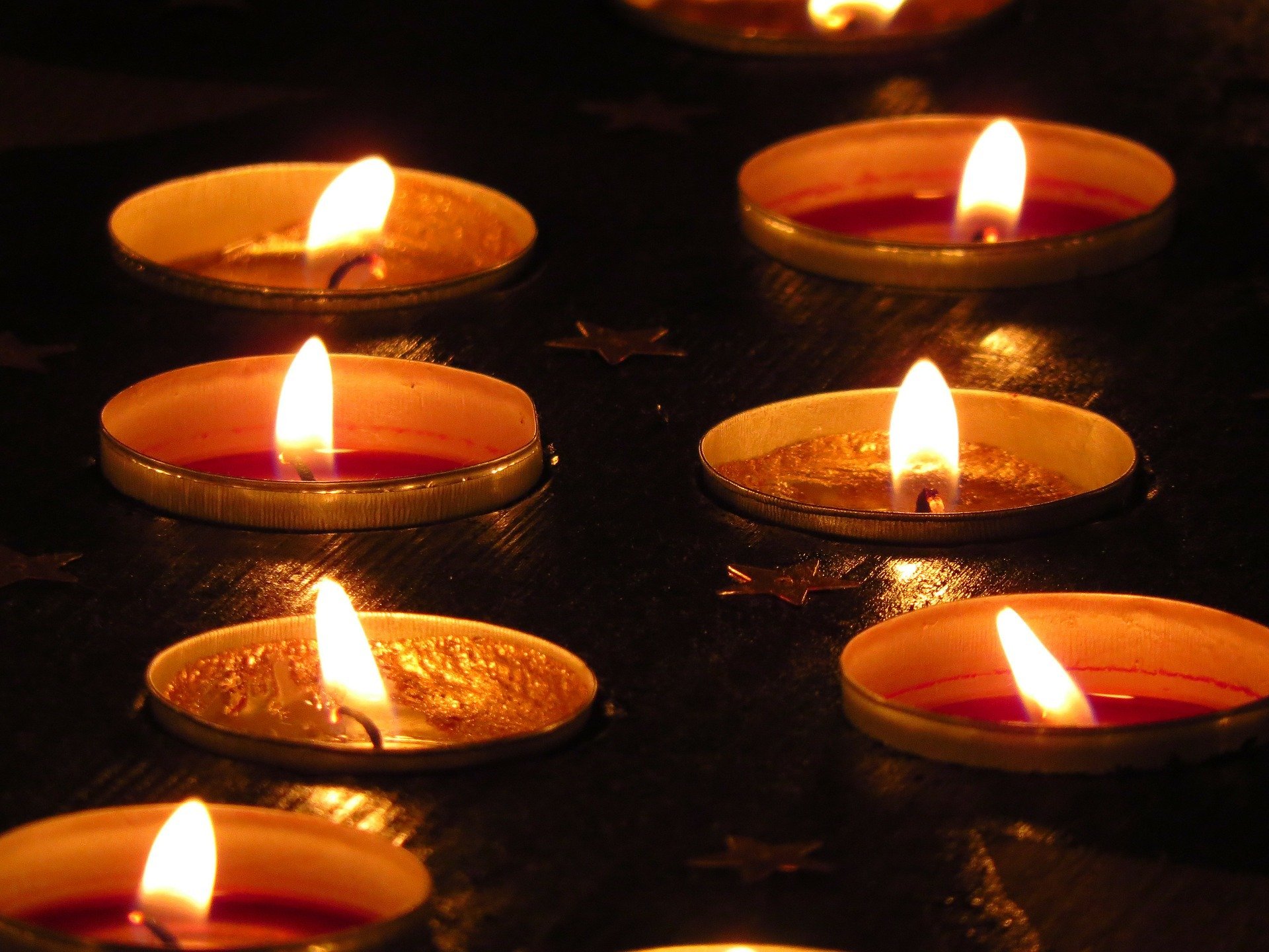 A bunch of lit tea light candles in a dark background | Photo: Pixabay/Hans Braxmeier