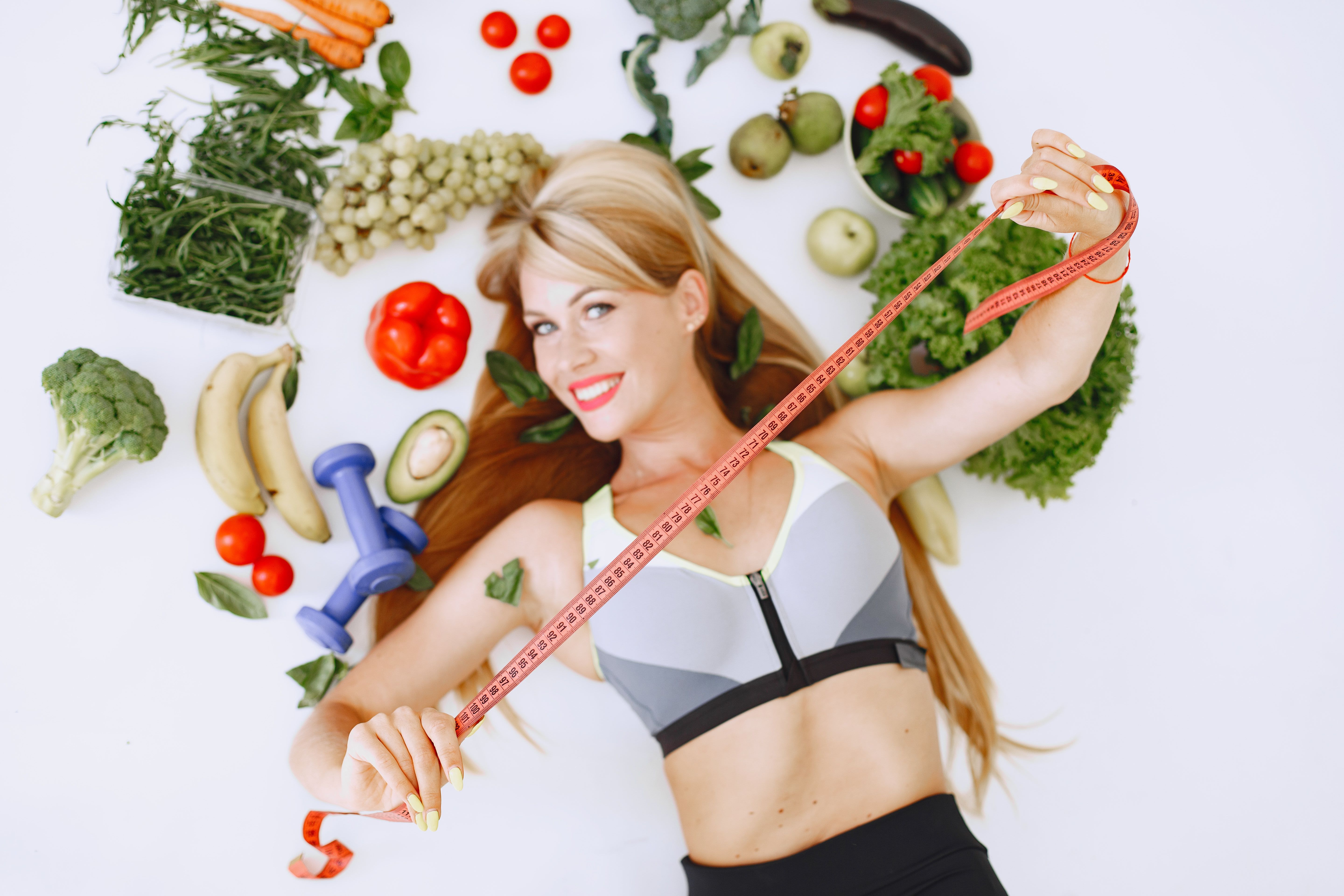 Woman holding a measuring tape while surrounded by fruits and vegetables | Source: Pexels
