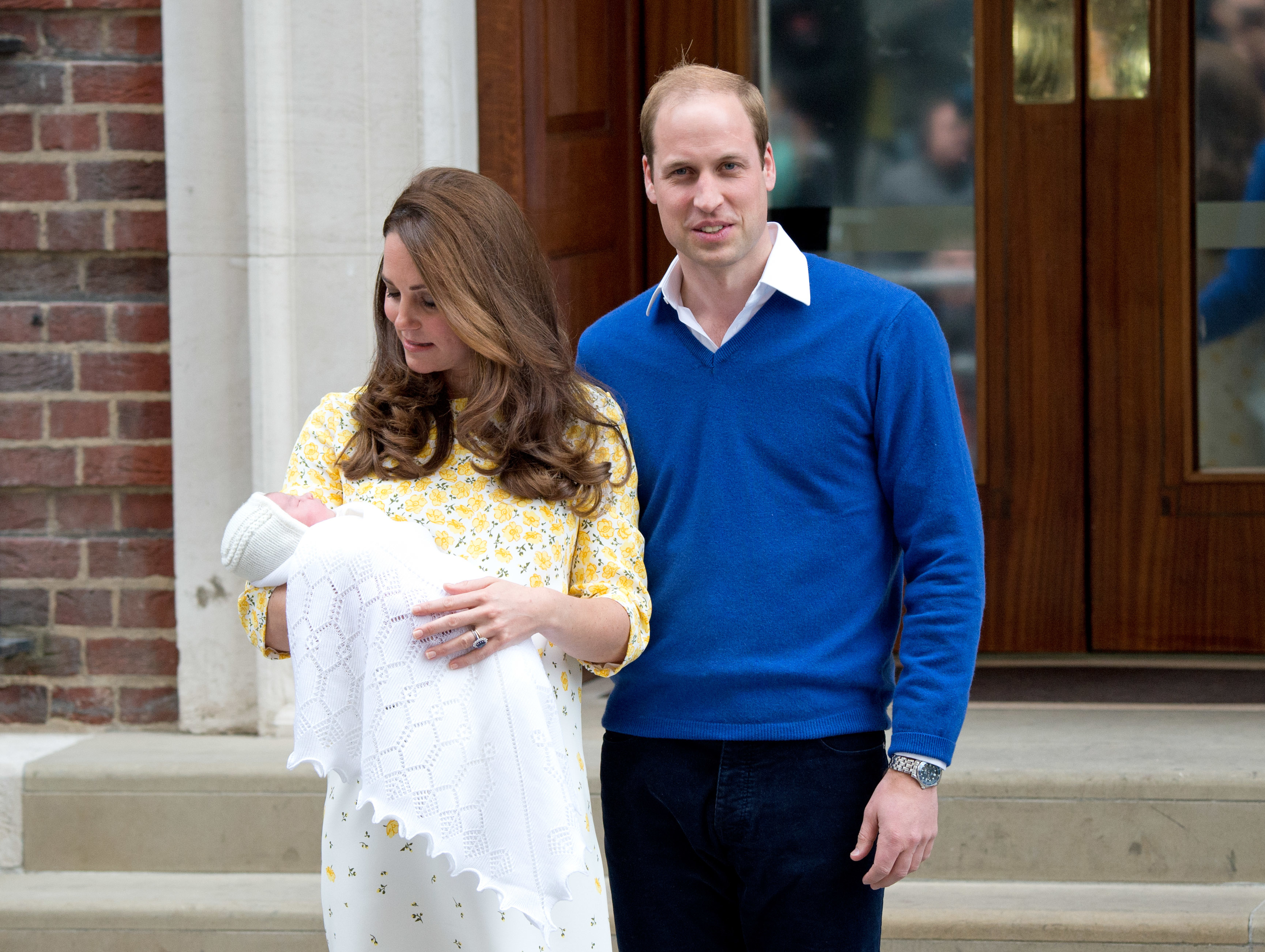 Catherine, dressed in a yellow floral frock, cradles a swaddled newborn Charlotte on the steps of the Lindo Wing at St Mary's Hospital, London, as William stands proudly at her side — the couple's first public appearance with their daughter, on 2 May 2015.