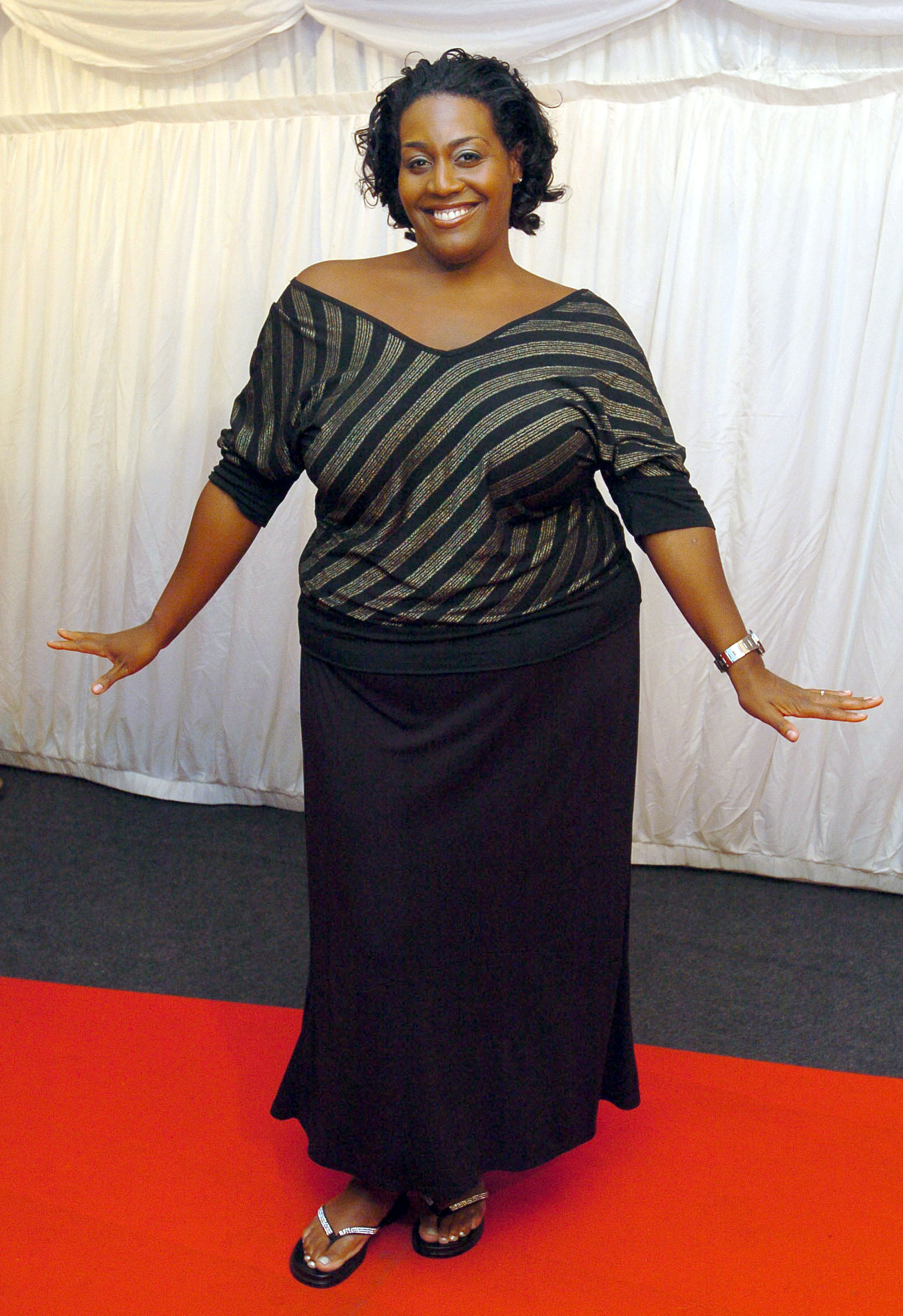 Alison Hammond flashes a dazzling smile as she steps out for ITV's "Hell's Kitchen" bash at Brick Lane, London, on 3 June 2004. Dressed in a flowing black skirt and a flirty off-the-shoulder striped top, she throws her arms out in a playful pose, soaking up the spotlight on the red carpet.