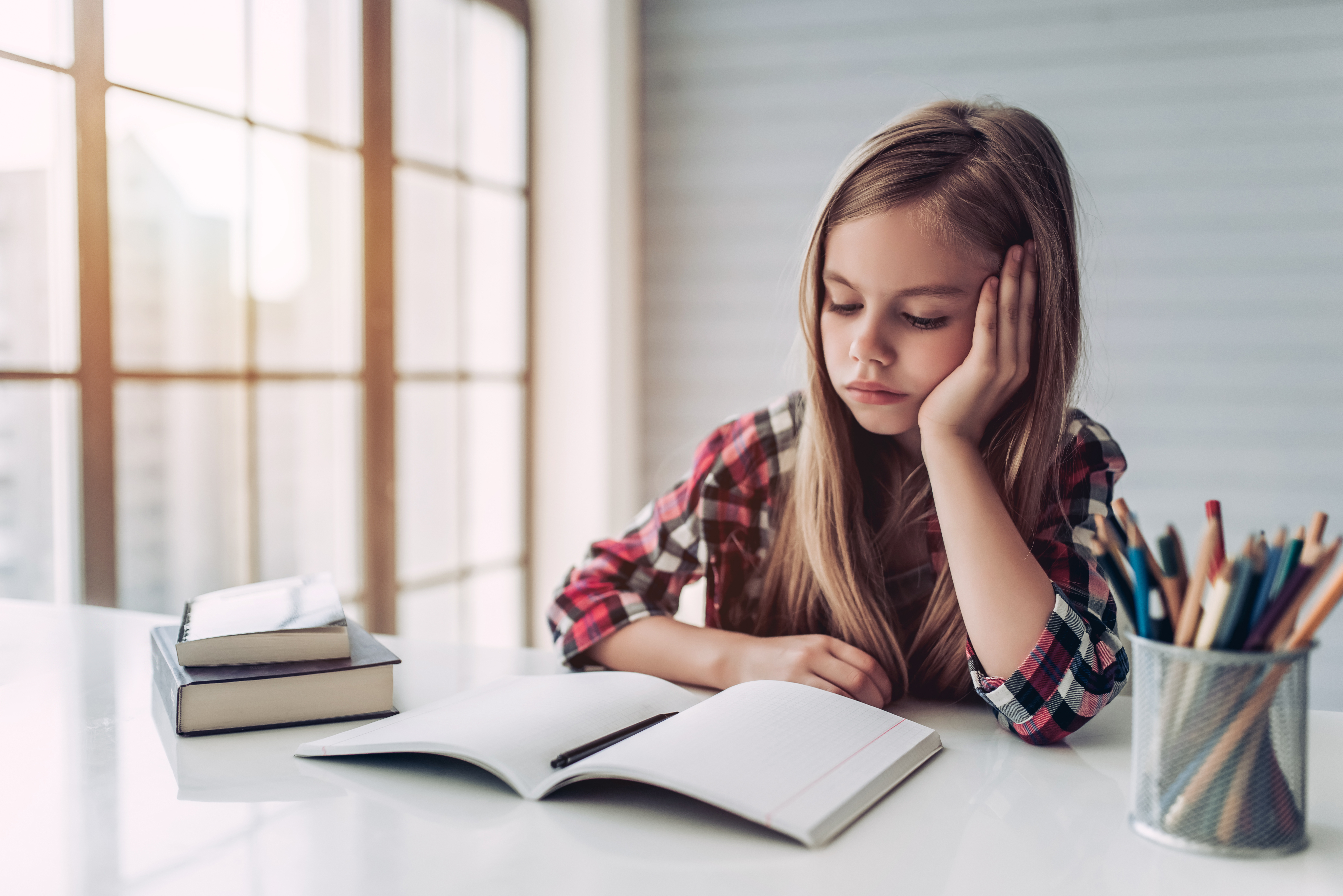 A young sad young girl staring at a book on her desk | Source: Shutterstock