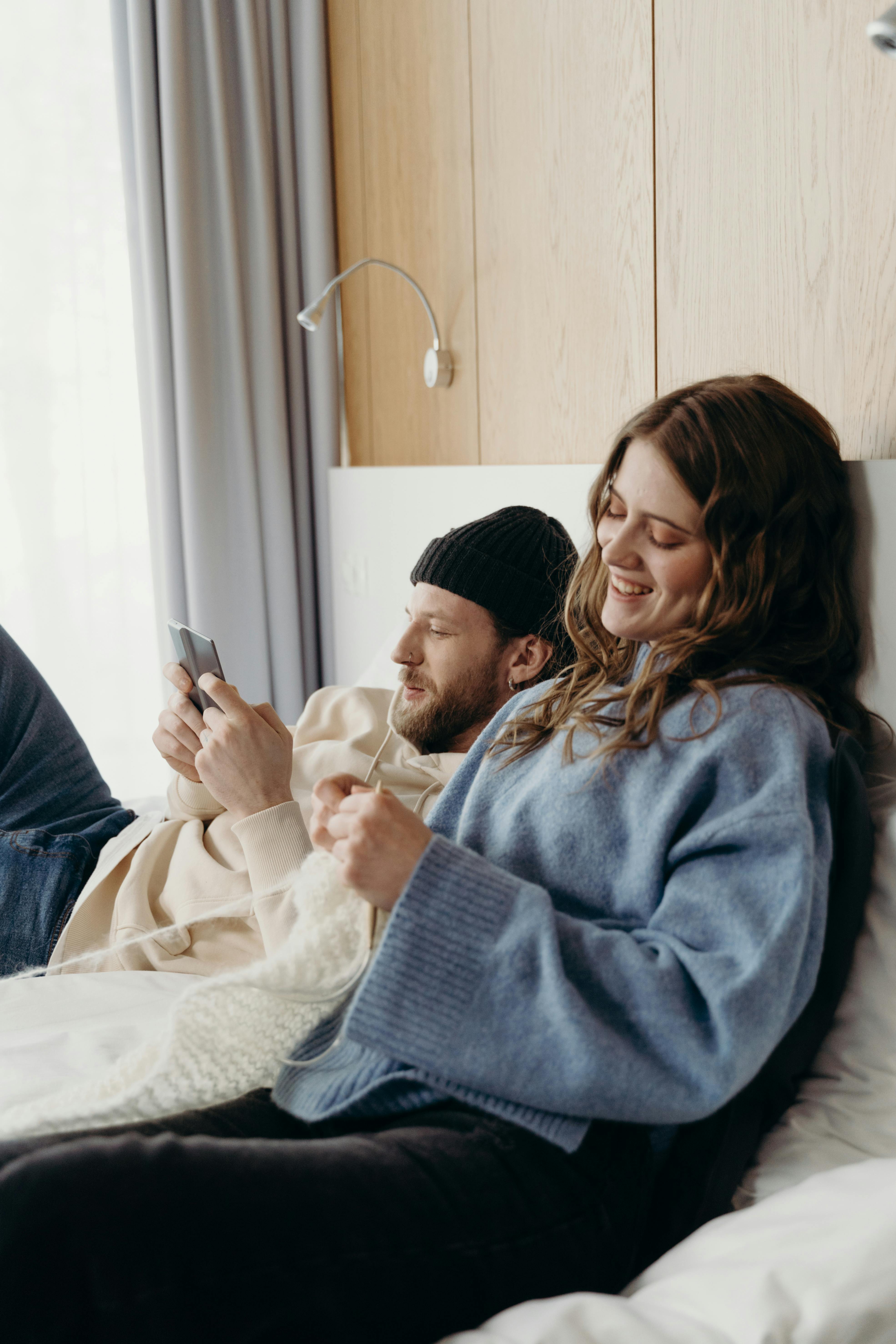 A happy woman knitting while her husband uses his phone | Source: Pexels