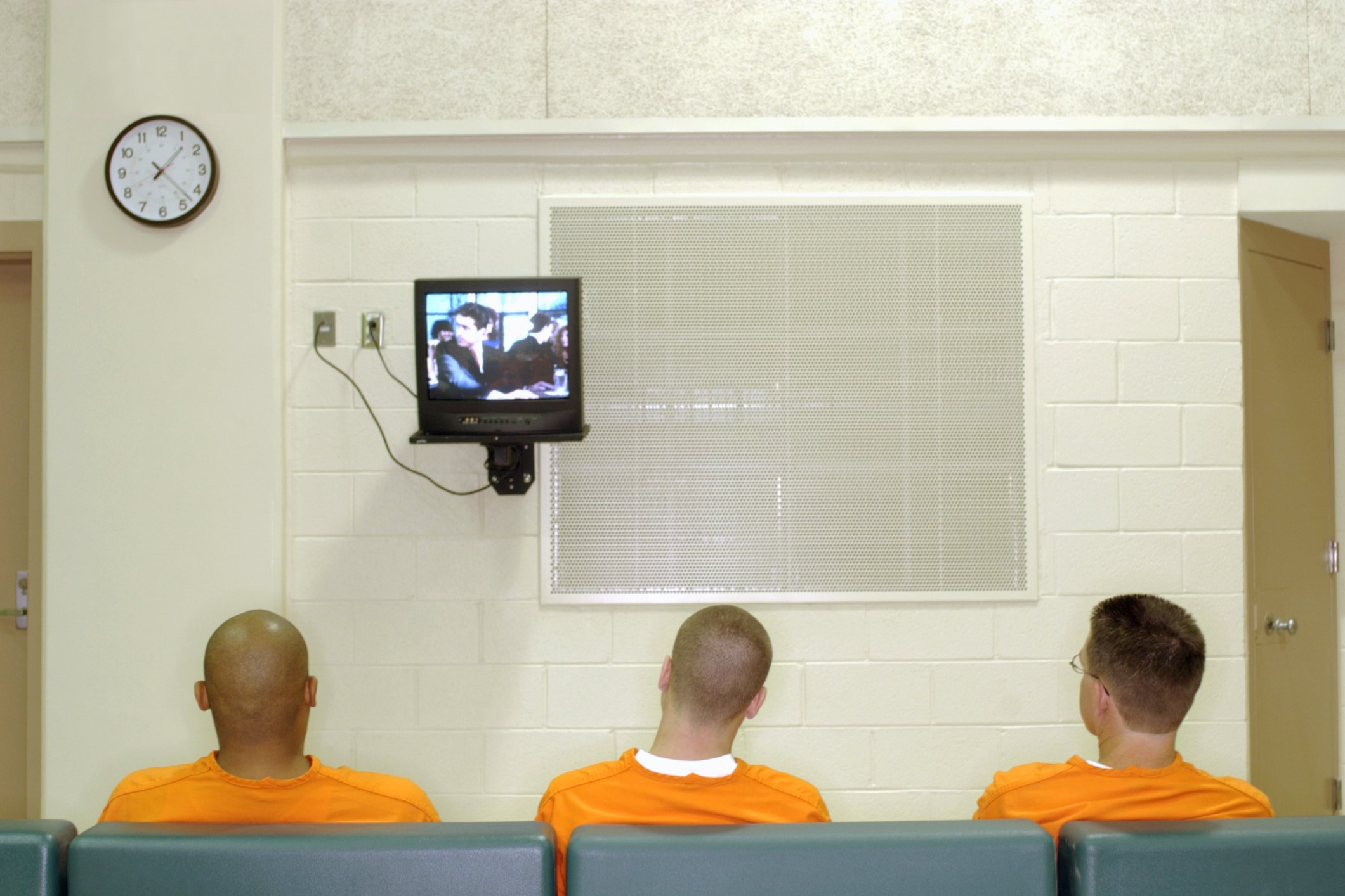 Three inmates seated in prison watching TV. | Photo: Getty Images