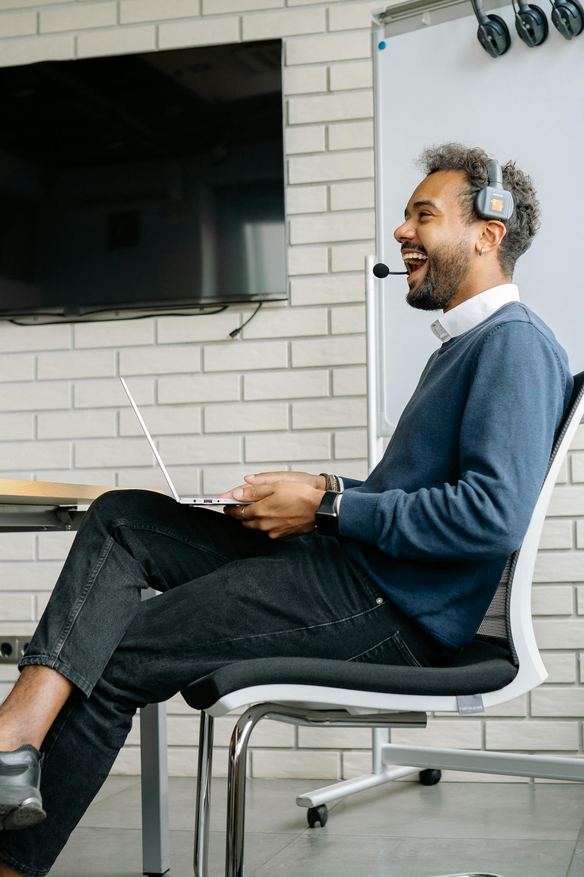 A man laughs while sitting on a chair in an office setting | Source: Pexels