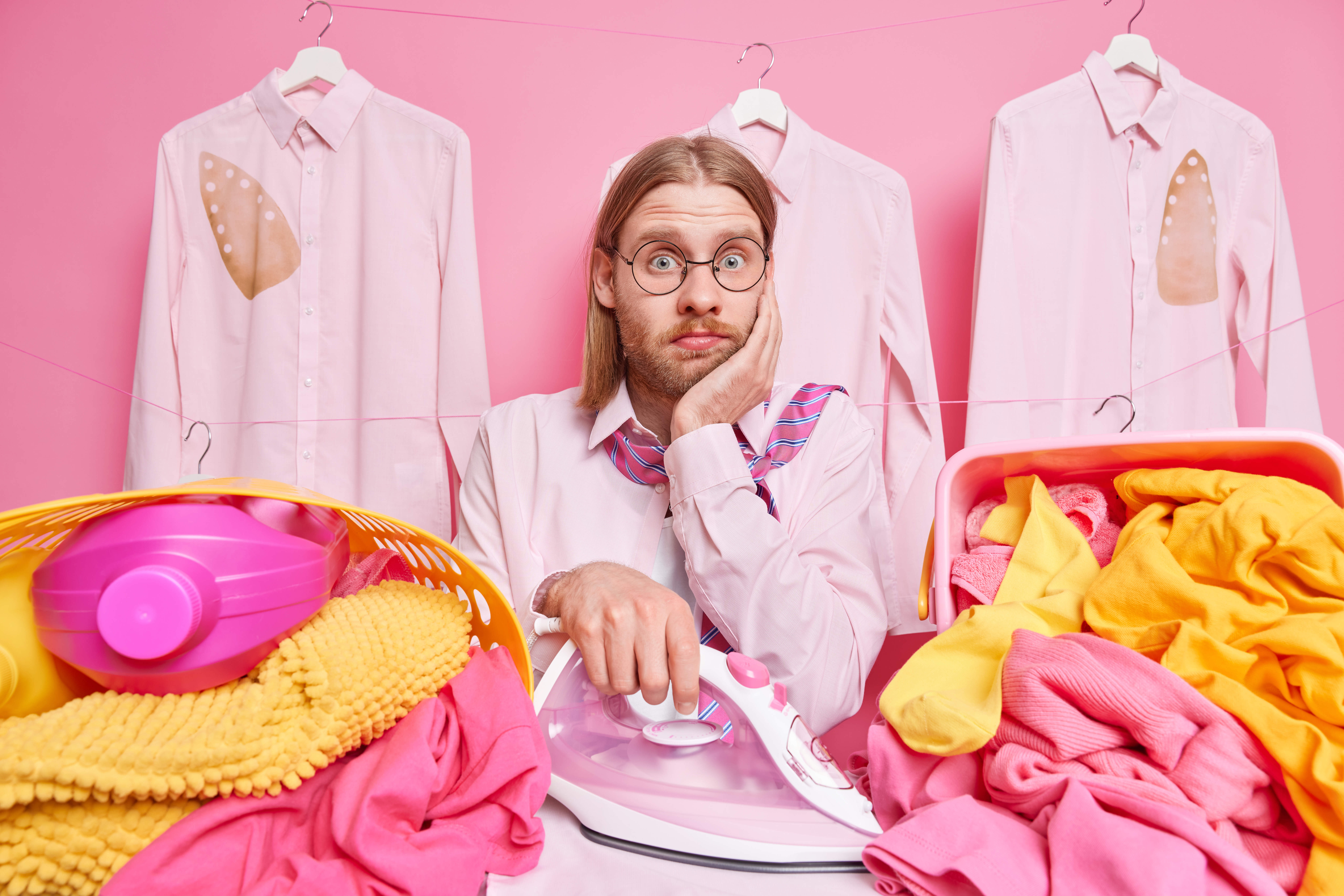 Man holding an iron in the midst of pink and yellow laundry | Source: wayhomestudio on Freepik