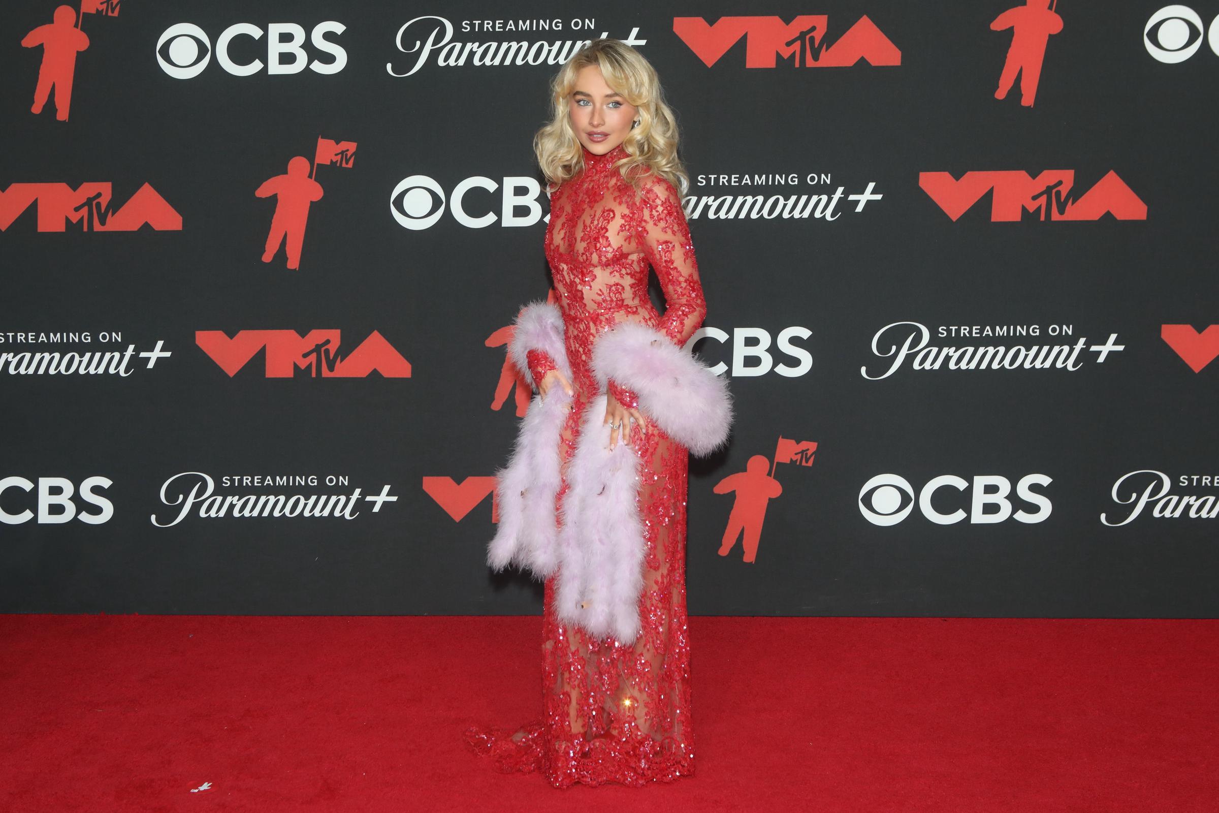 Sabrina Carpenter turns heads at the event in a sheer red, sequin gown paired with a pink, feather-trimmed stole, channeling vintage glamor.