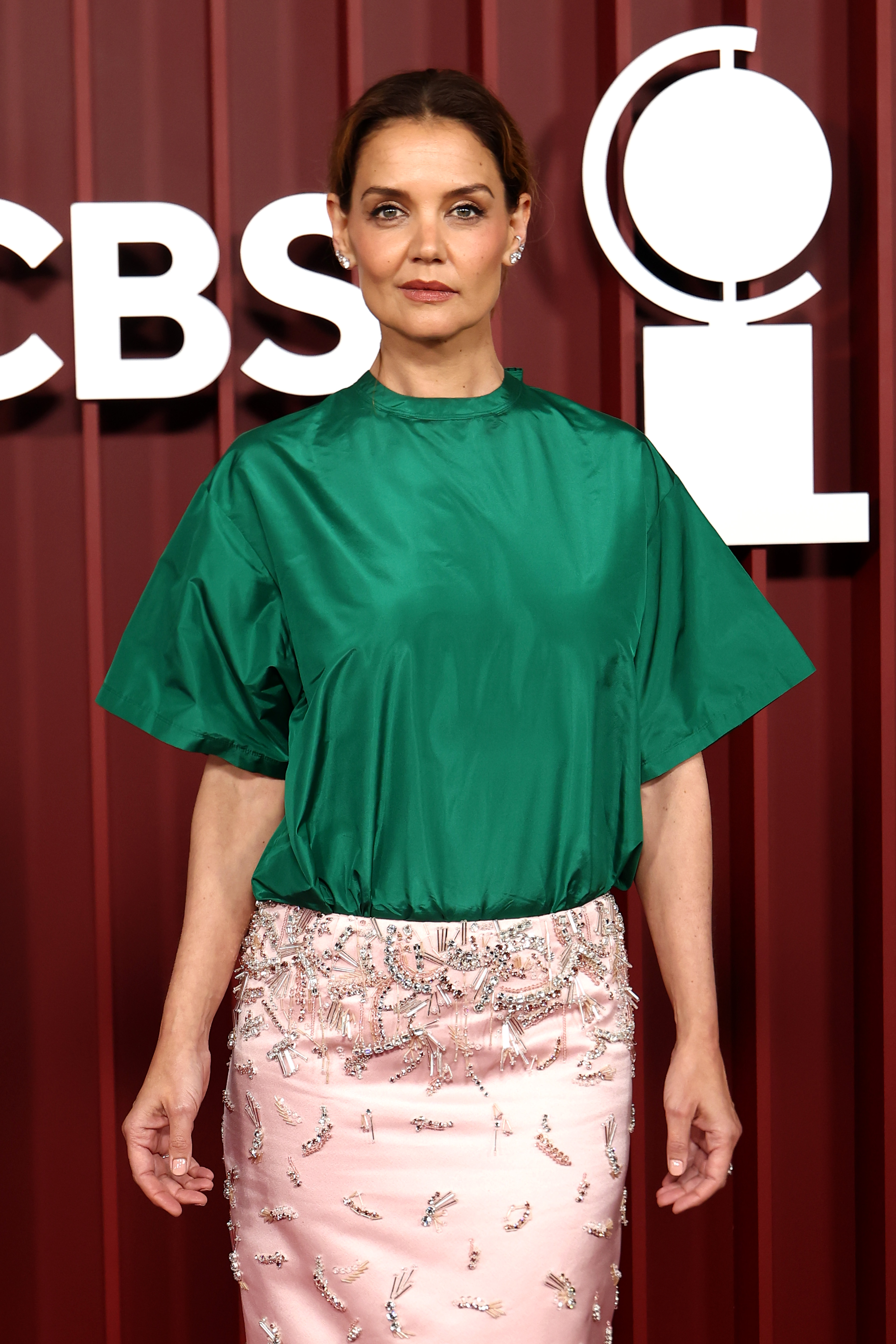 Katie Holmes stands front and center in a structured green top and pale pink skirt detailed with delicate beadwork. Her composed expression and clean styling let the striking contrast of textures and colors do all the talking.